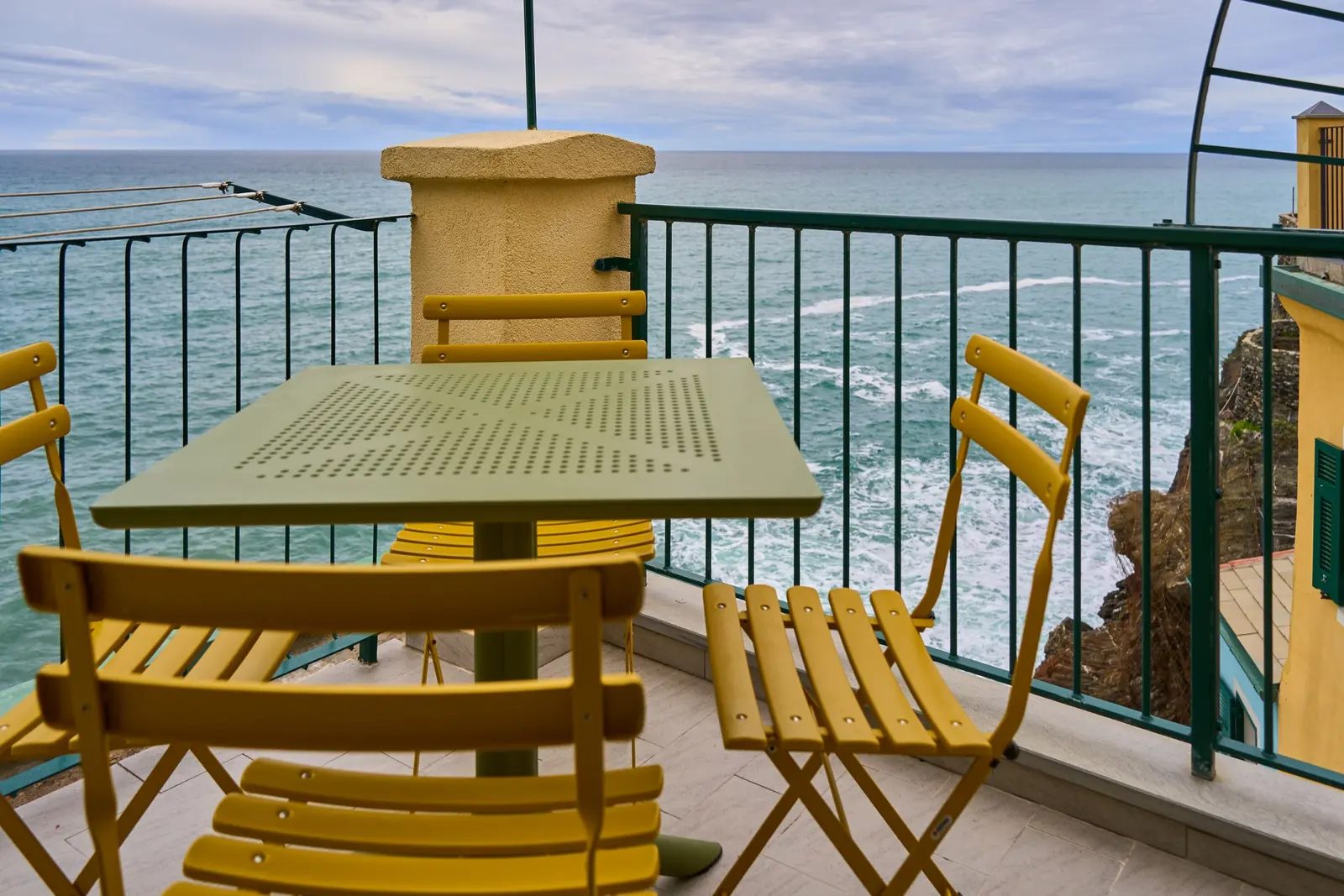 Un terrazzino con sedie gialle pieghevoli e la ringhiera verde affacciata sul mare