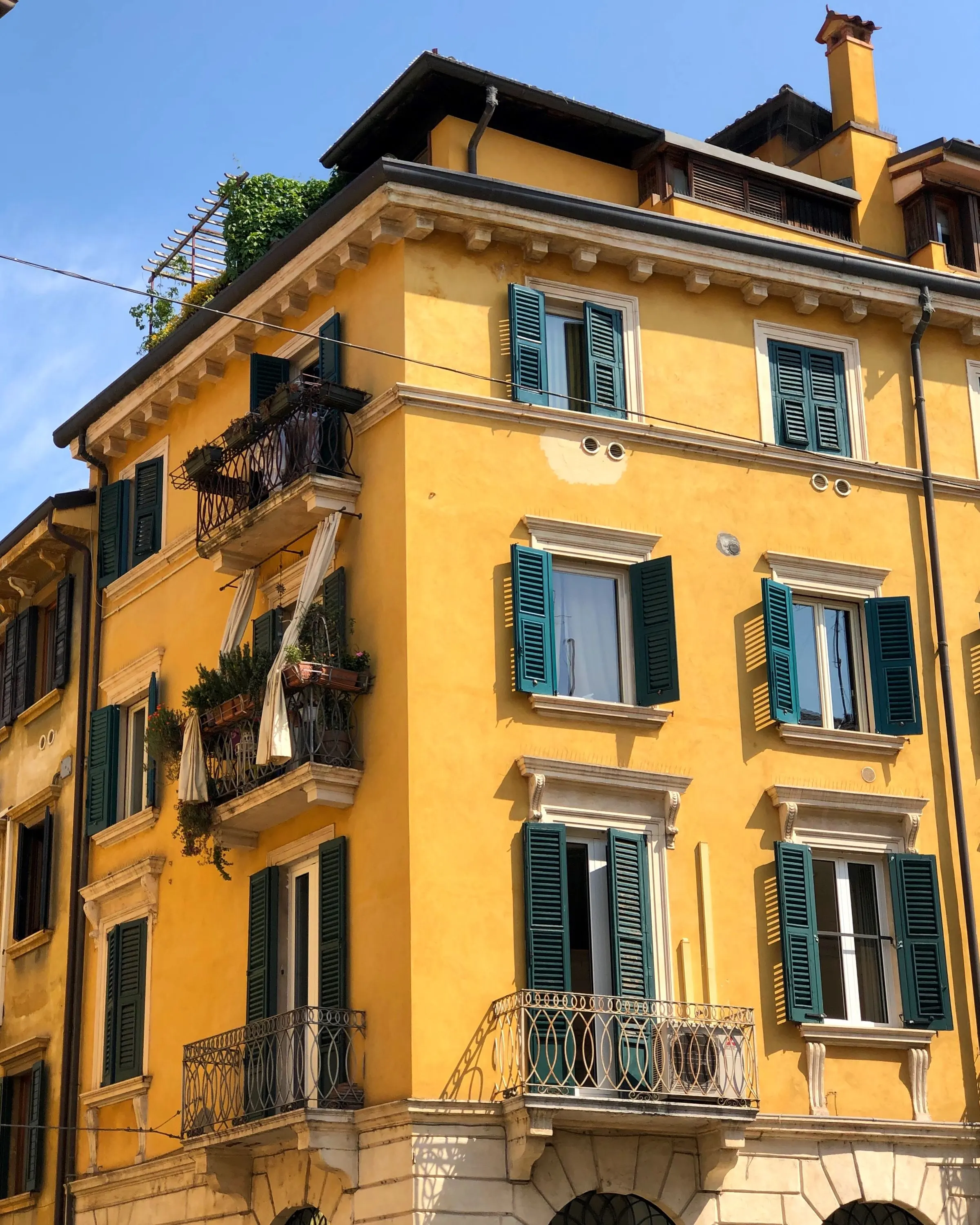 Un palazzo d'angolo giallo con persiane verdi e balconi in ferro, sotto un cielo sereno