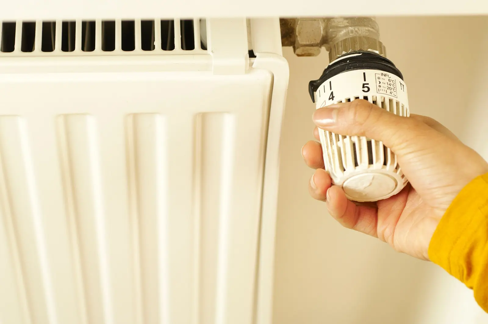 Una mano regola la valvola termostatica di un termosifone bianco
