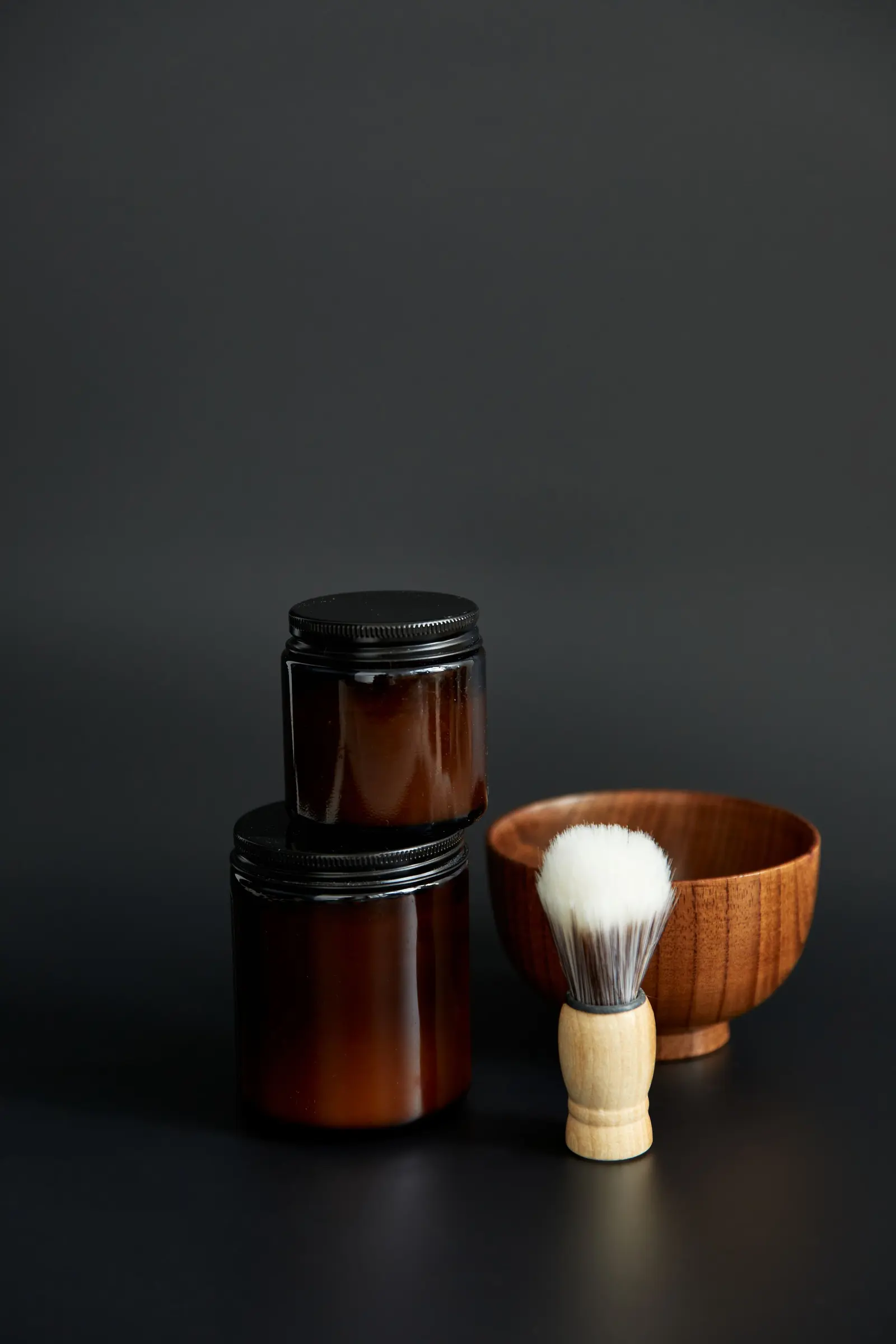 Due vasetti ambrati, una ciotola di legno e un pennello su fondo nero