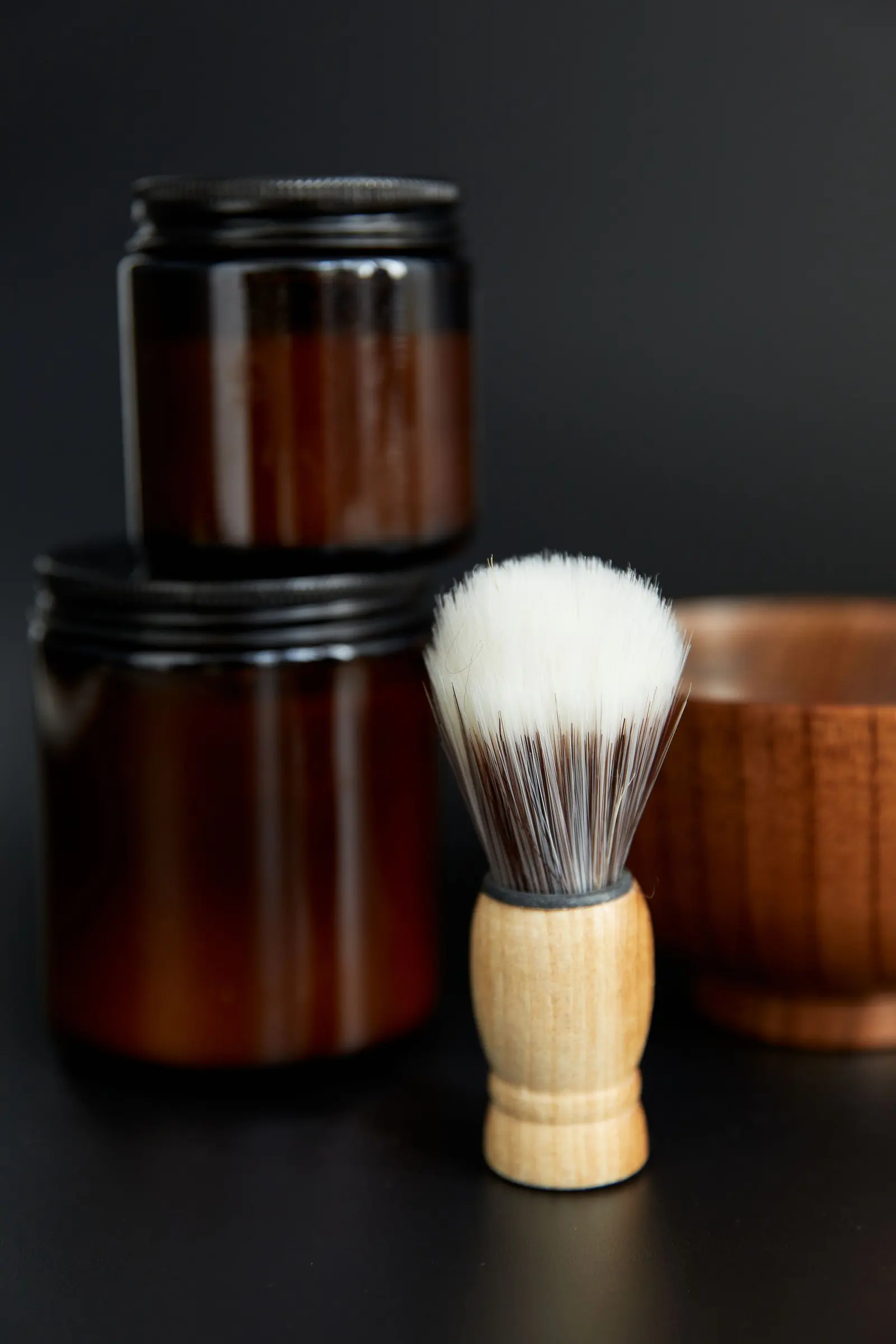 Pennello da barba con manico di legno accanto a vasetti scuri