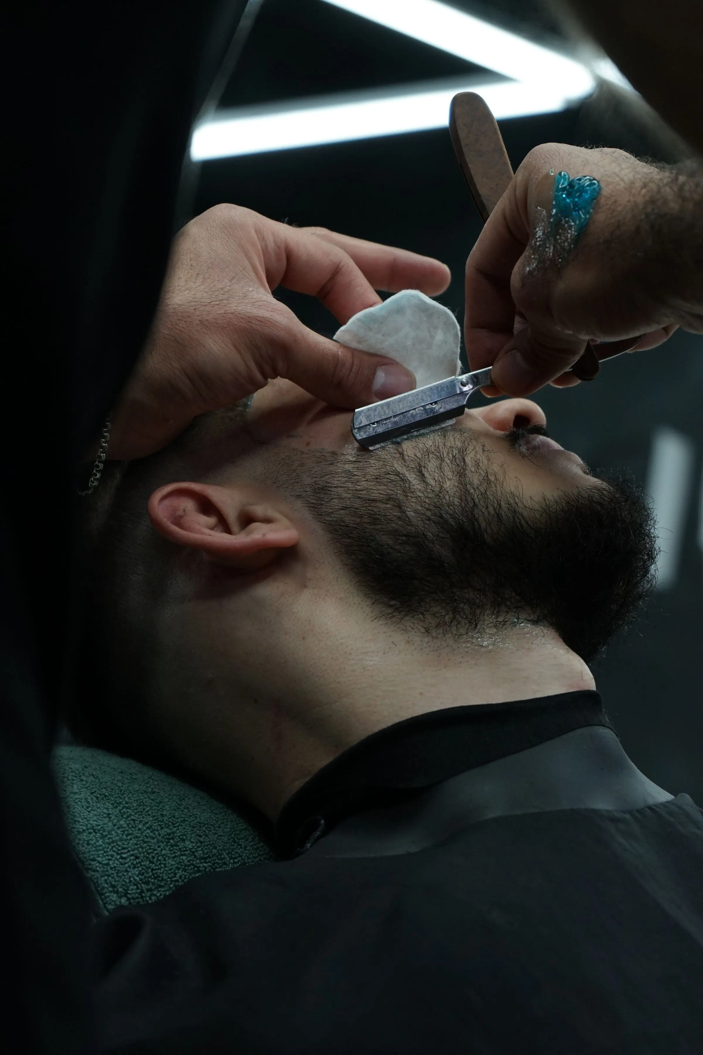 Il barbiere rade la barba di un cliente con il rasoio a mano libera, in luce bassa