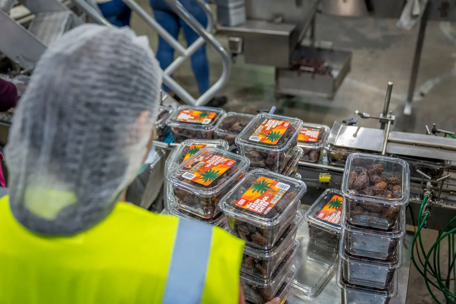 Un'operatrice con cuffia controlla vaschette trasparenti di datteri su una linea in acciaio inox