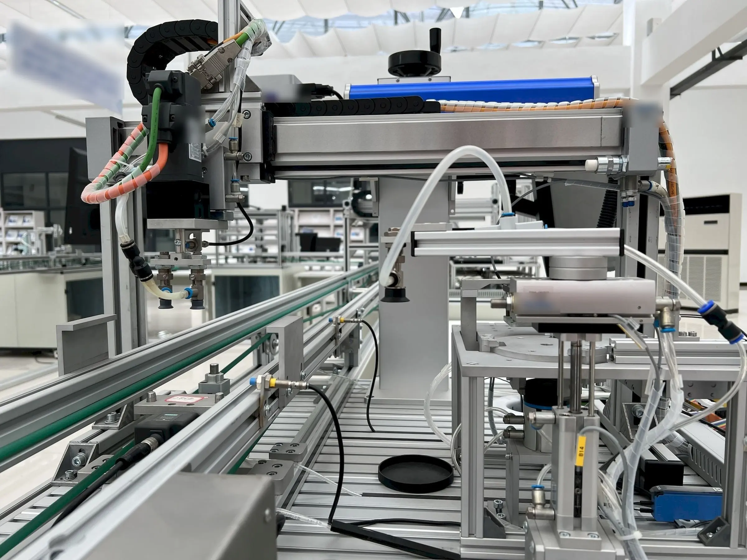 Una linea automatica in un reparto luminoso: portale con pinza pneumatica sopra un nastro trasportatore in alluminio