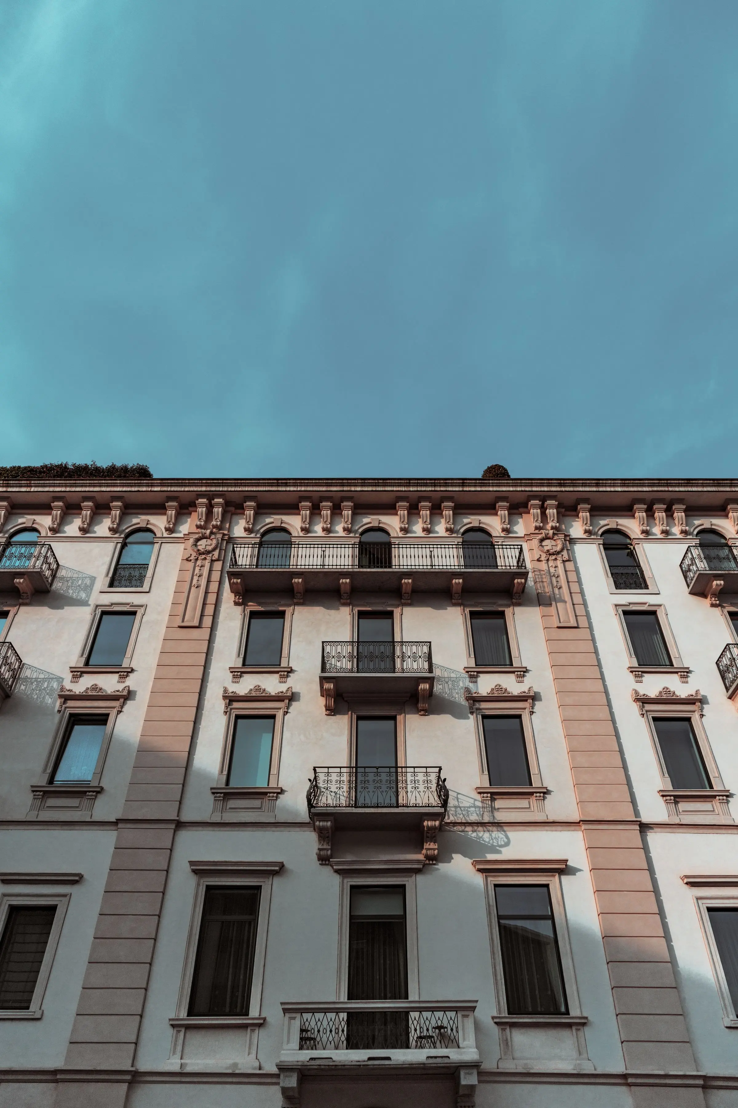 Facciata di un palazzo d'epoca color rosa e crema, con balconi in ferro battuto, vista dal basso