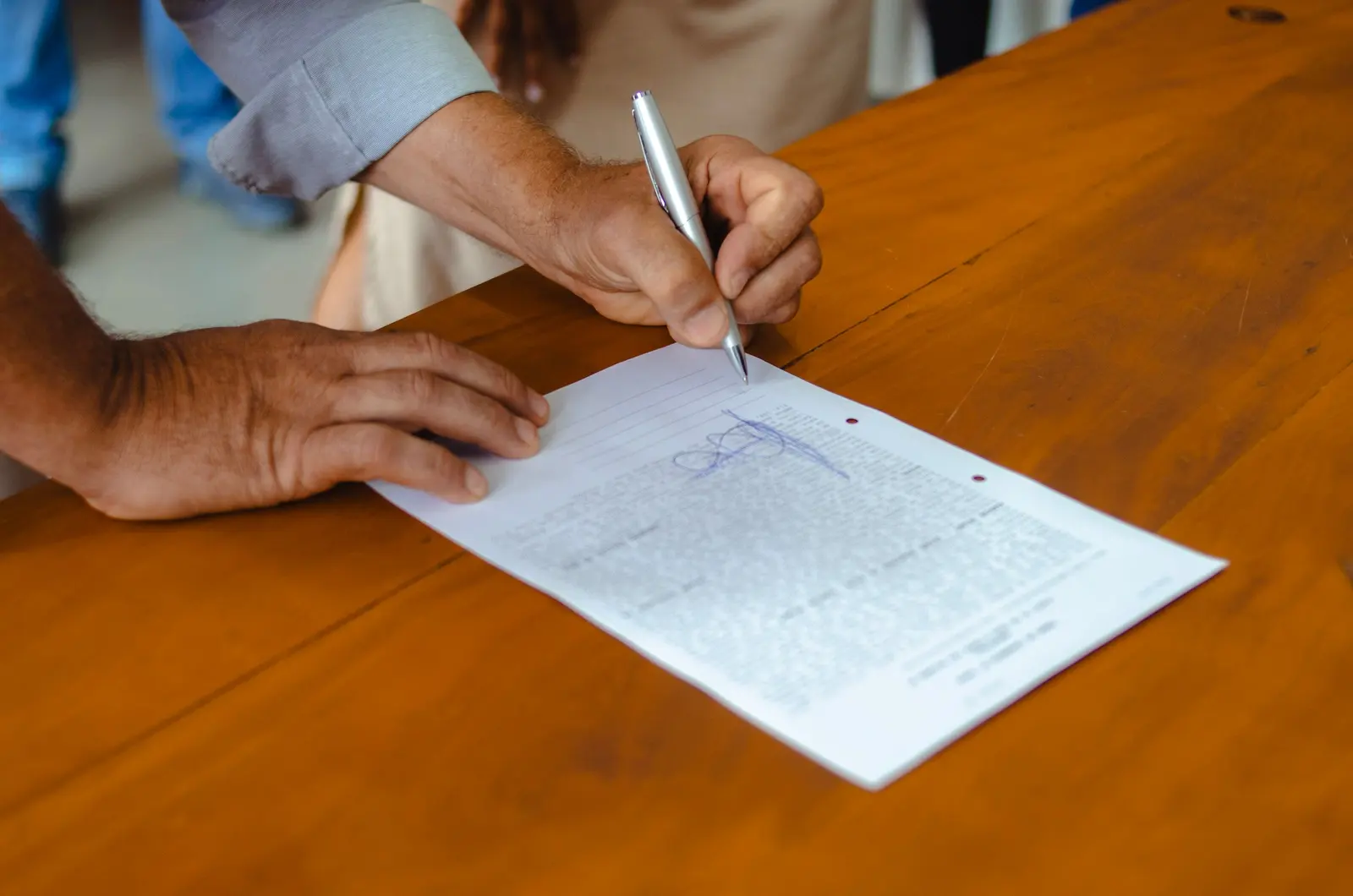 Una mano firma un foglio appoggiato su un tavolo di legno