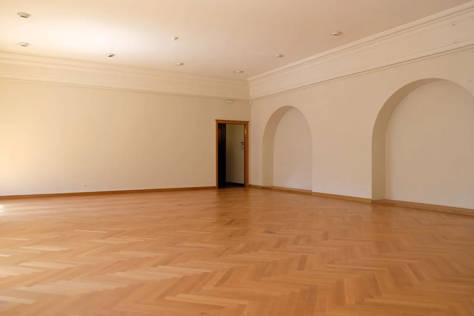Salone vuoto con parquet a spina di pesce e archi, luce calda dalle finestre
