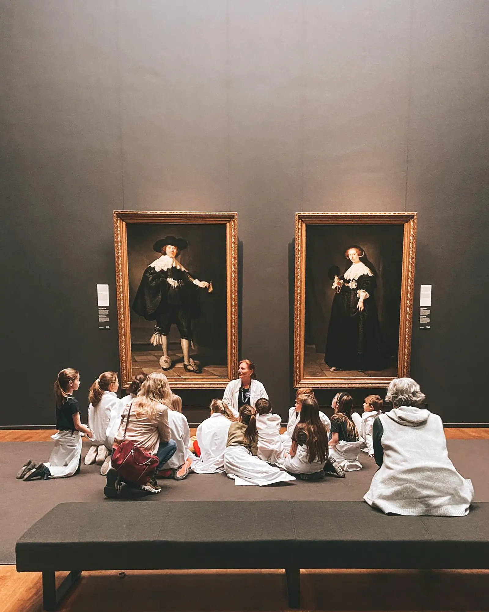 Una classe seduta per terra con la guida davanti a due grandi ritratti in una sala di museo