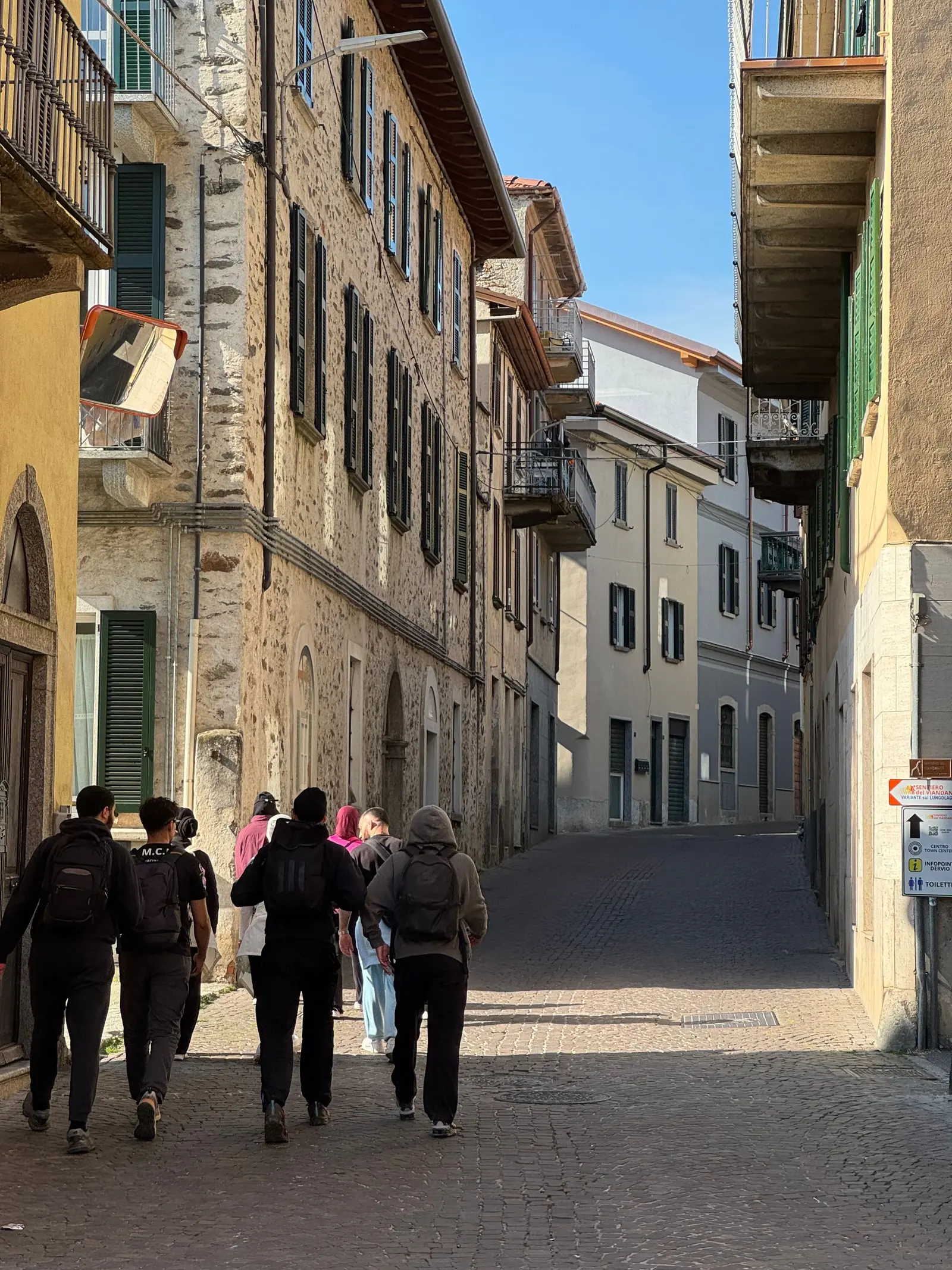 Un gruppo di ragazzi con gli zaini che cammina in un vicolo assolato di un centro storico