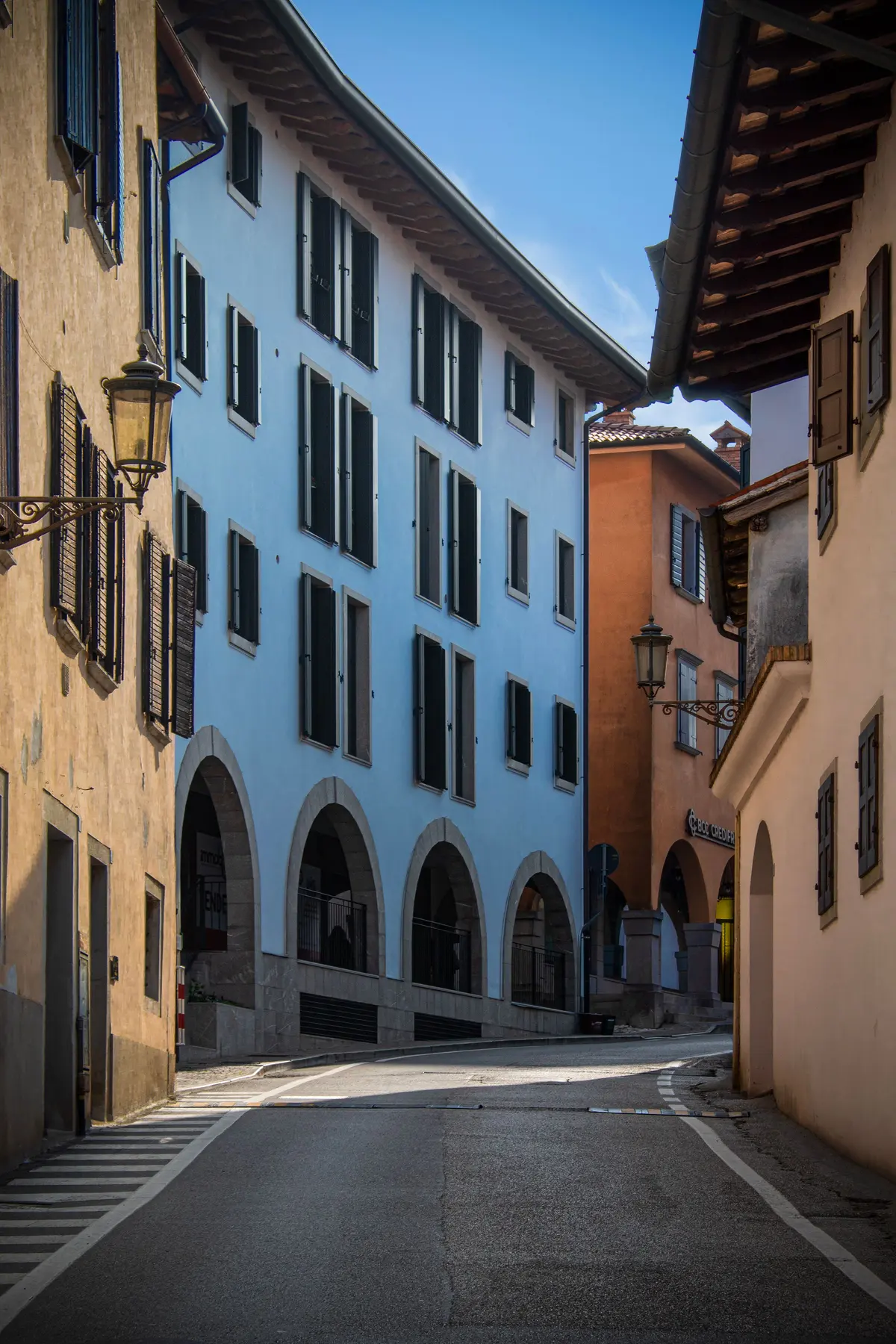 Una via di una cittadina del Nord con i portici e le facciate color pastello, sotto un cielo azzurro