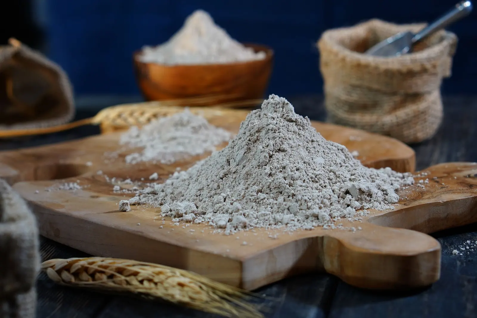 Un mucchio di farina su un tagliere di legno, con spighe e un sacchetto di juta