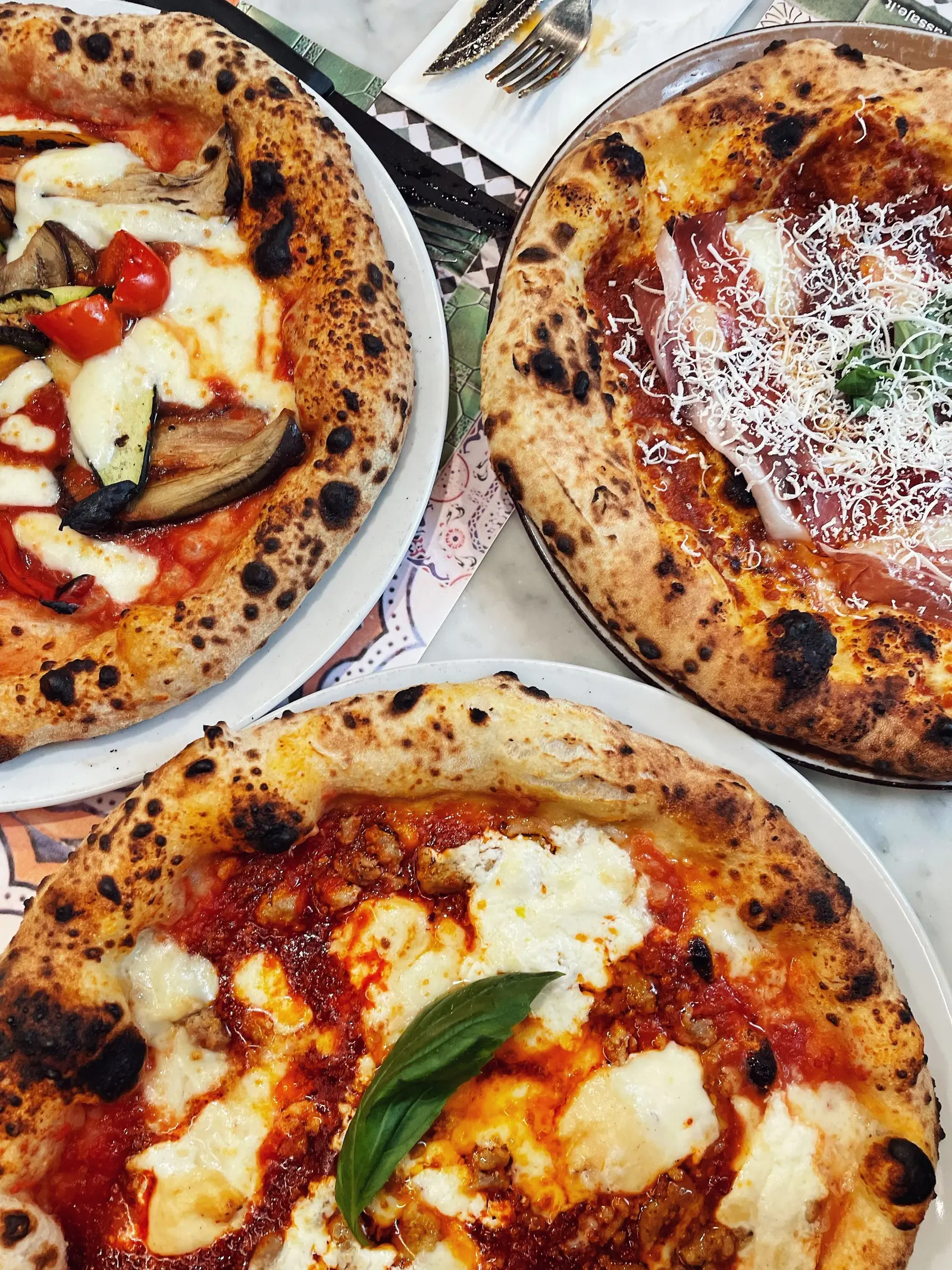 Tre pizze napoletane diverse su piatti bianchi, viste dall'alto