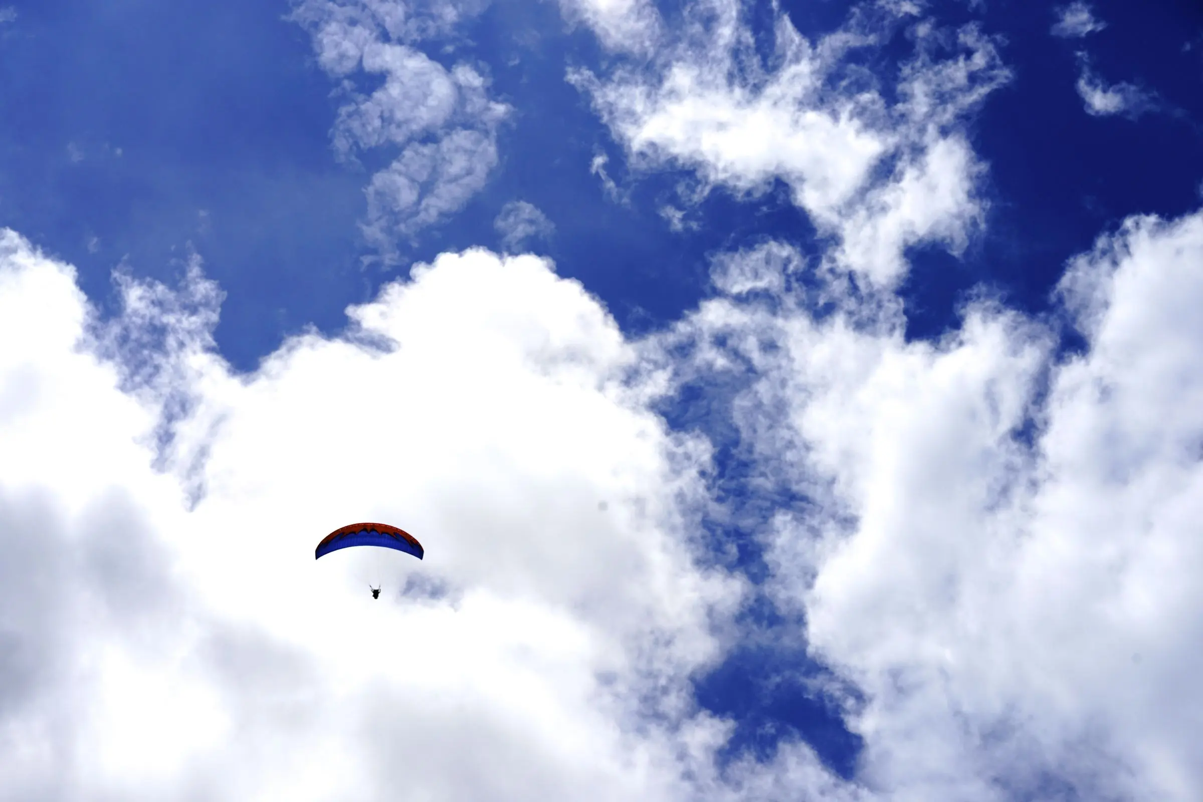 Un parapendio piccolo nel cielo blu, in mezzo a grandi nuvole bianche