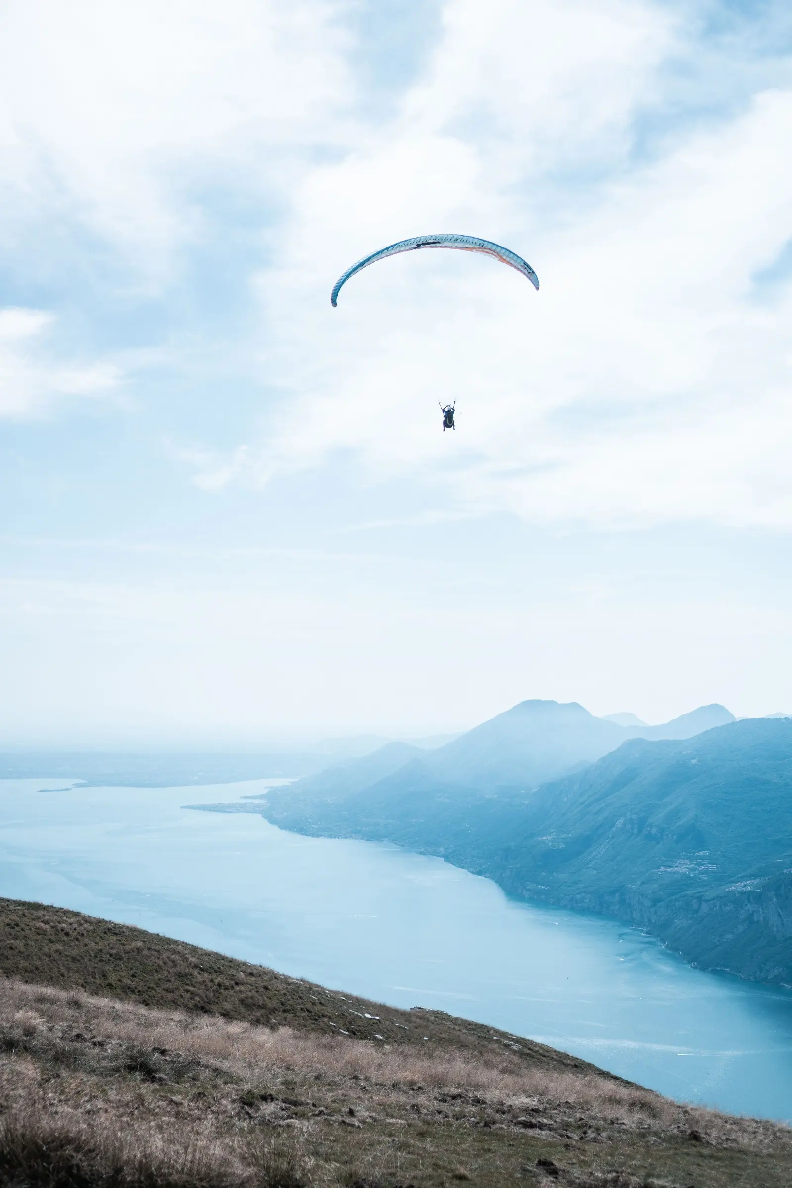 Una vela in volo sopra il lago lungo e stretto tra le montagne, nella foschia chiara