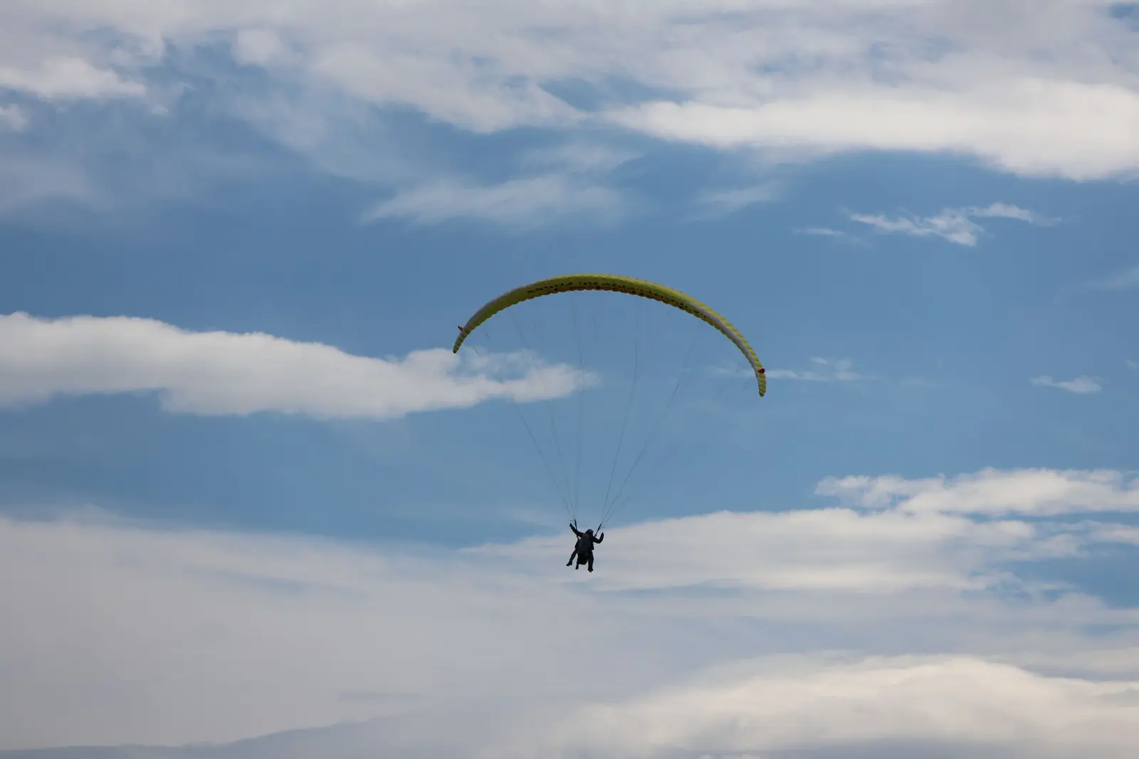 Un parapendio biposto lontano, in un cielo chiaro con nuvole sottili a strati