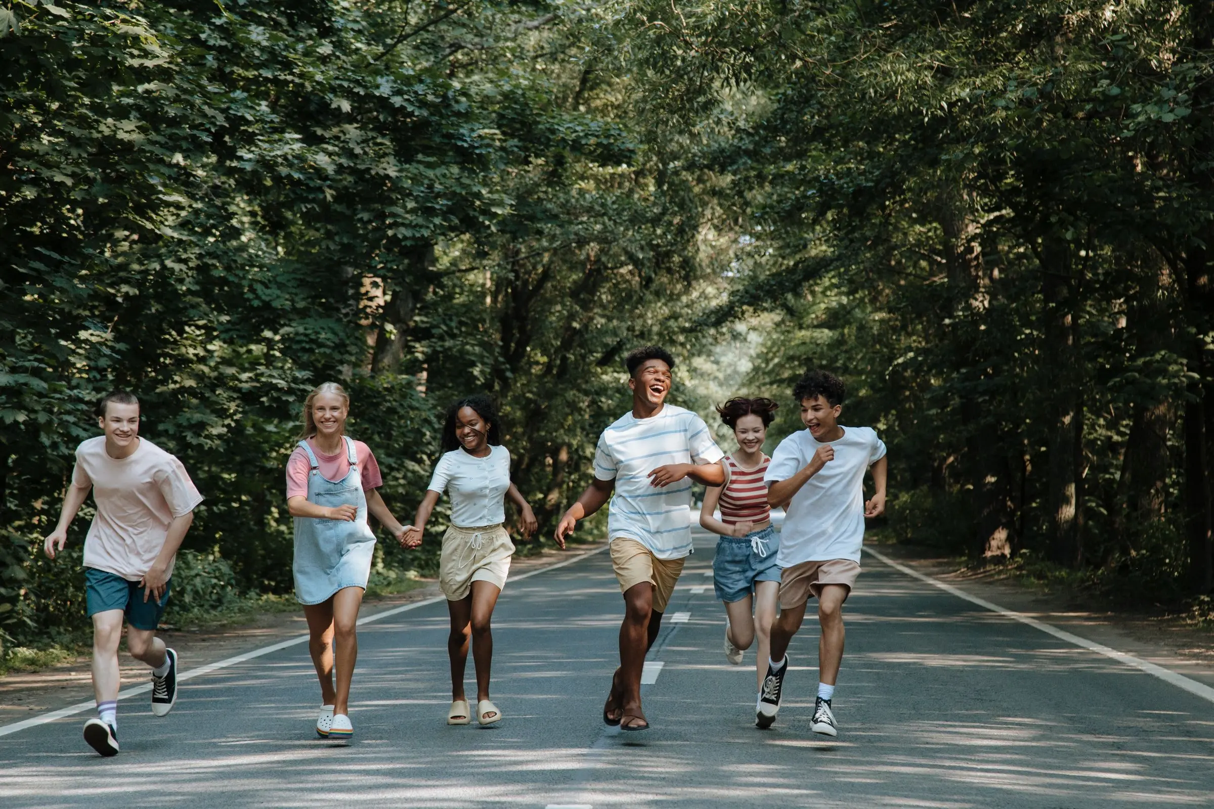 Un gruppo di ragazzi che corre ridendo su una strada tra gli alberi, in un pomeriggio d'estate