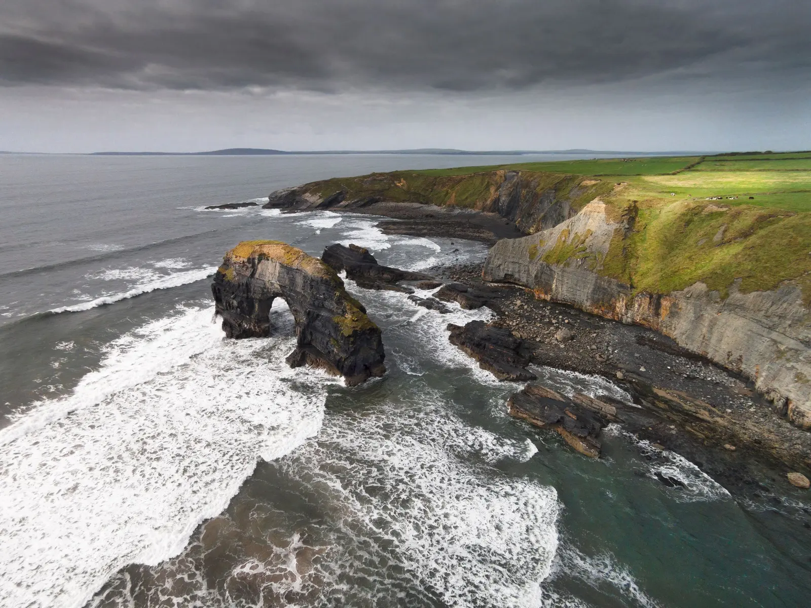Le scogliere verdi della costa ovest irlandese con un arco di roccia nell'oceano
