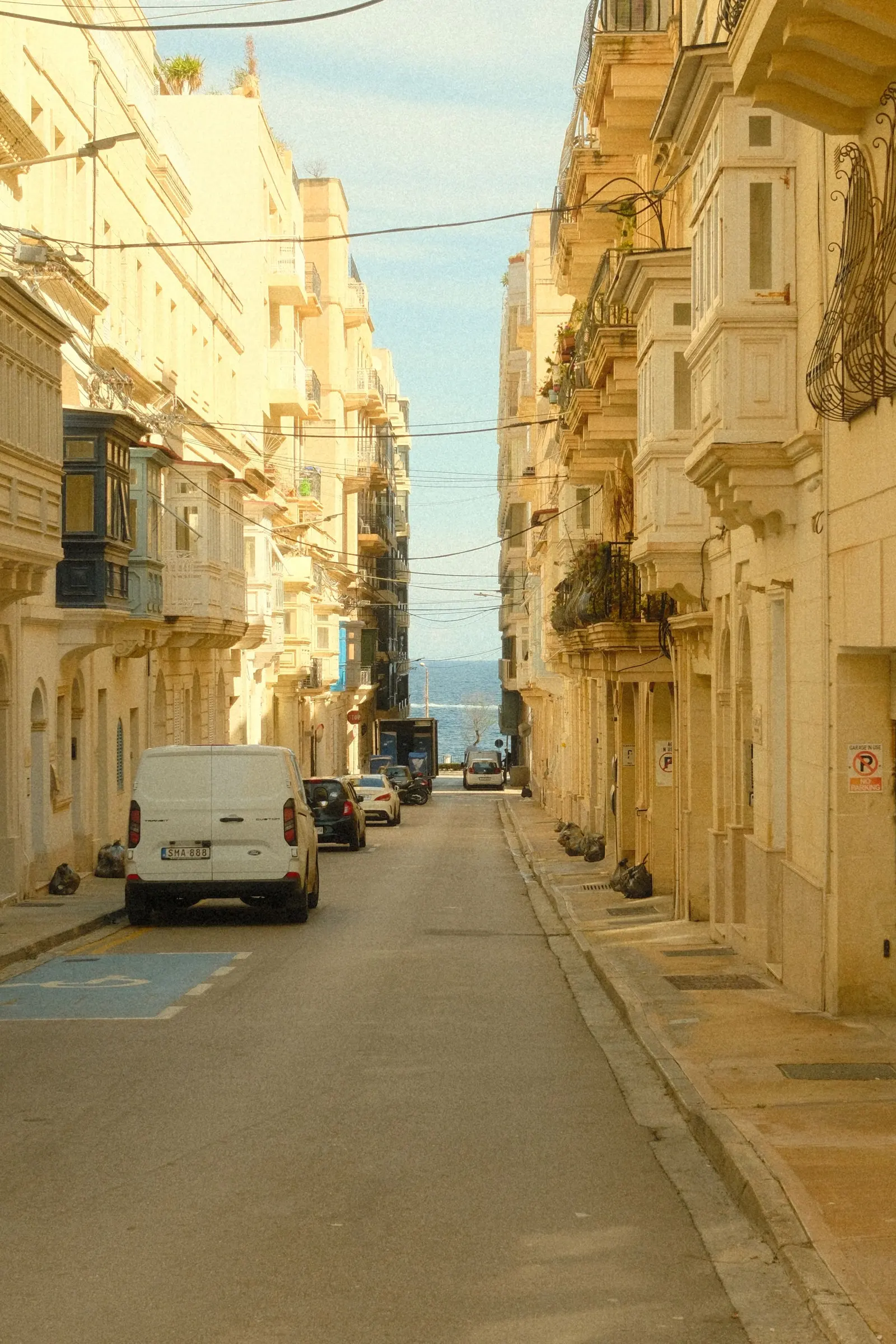 Una via di pietra chiara a Malta, con i balconi chiusi, che scende verso il mare