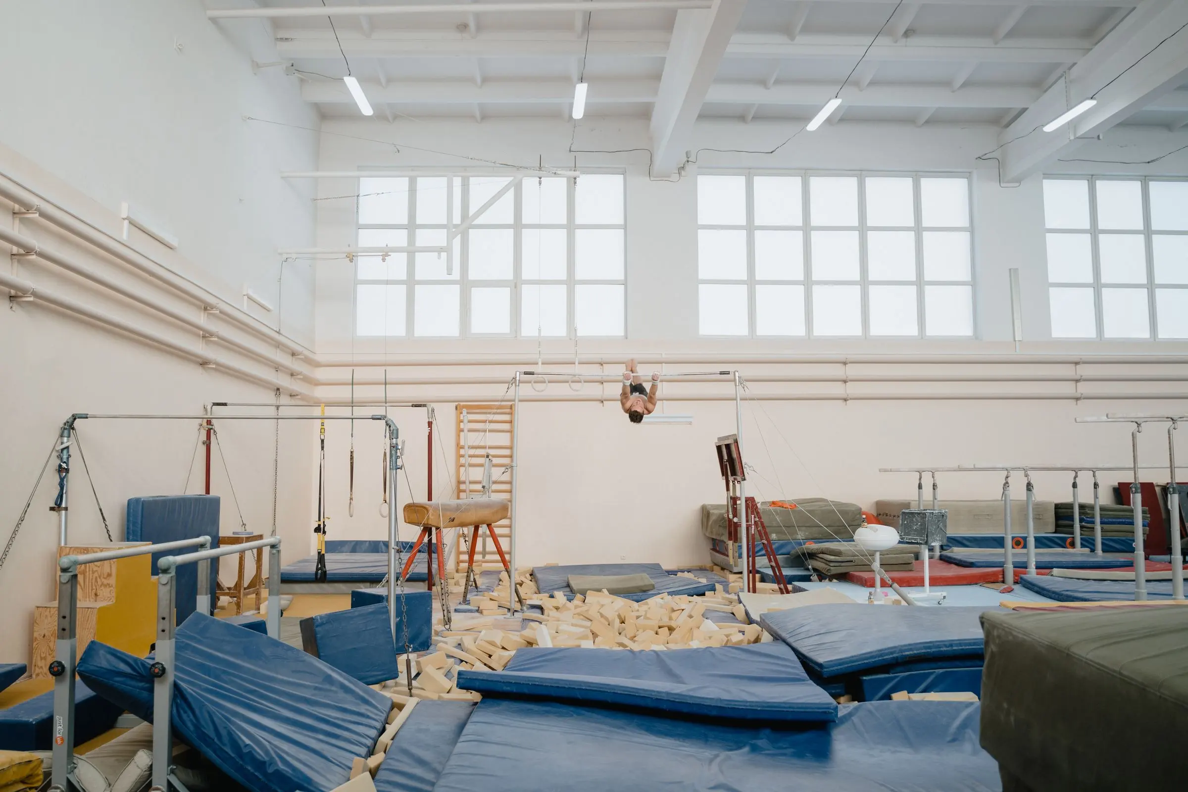 Palestra di ginnastica artistica con materassi blu sotto gli attrezzi e una fossa piena di blocchi di spugna