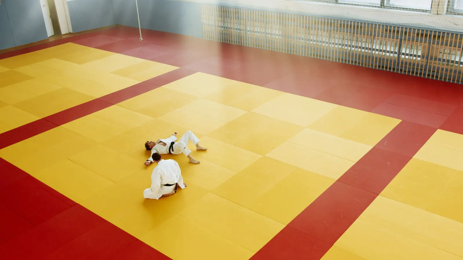 Sala con il tatami giallo e la fascia rossa di sicurezza, due judoka in fondo