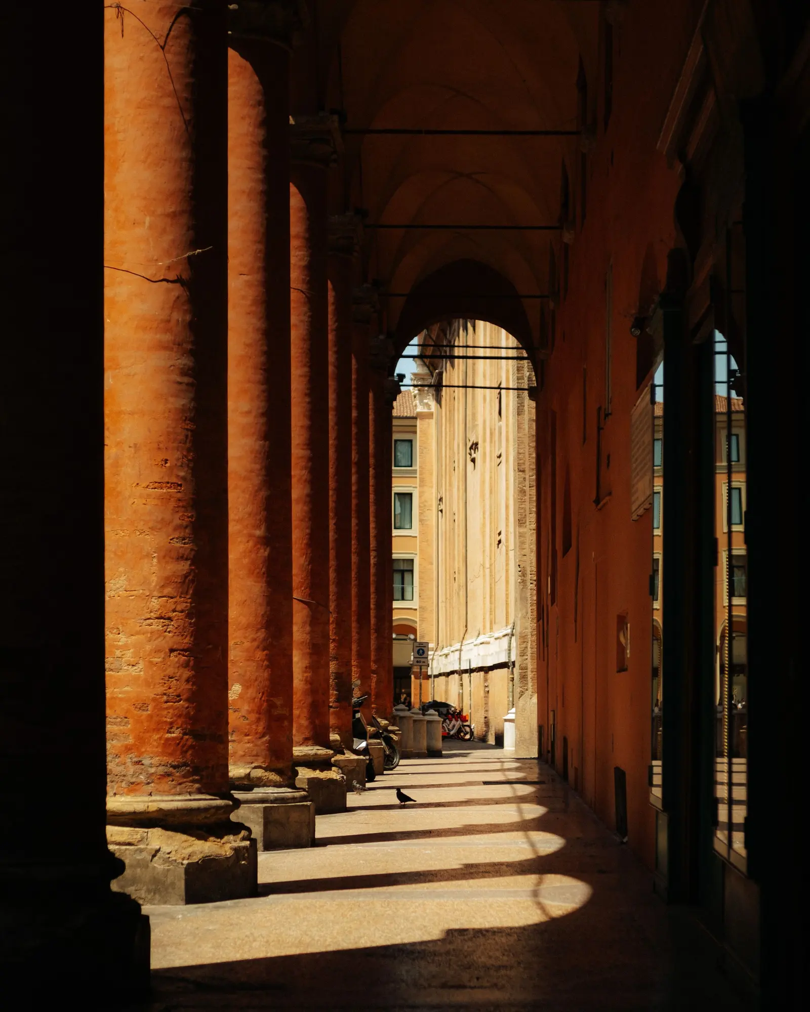 Un portico di Bologna al sole, con le ombre degli archi sul pavimento