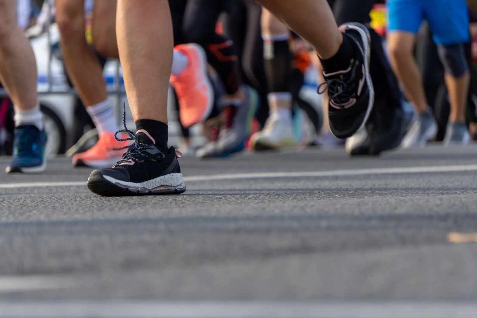 Primo piano basso delle gambe e delle scarpe di un gruppo di podisti in gara sull'asfalto