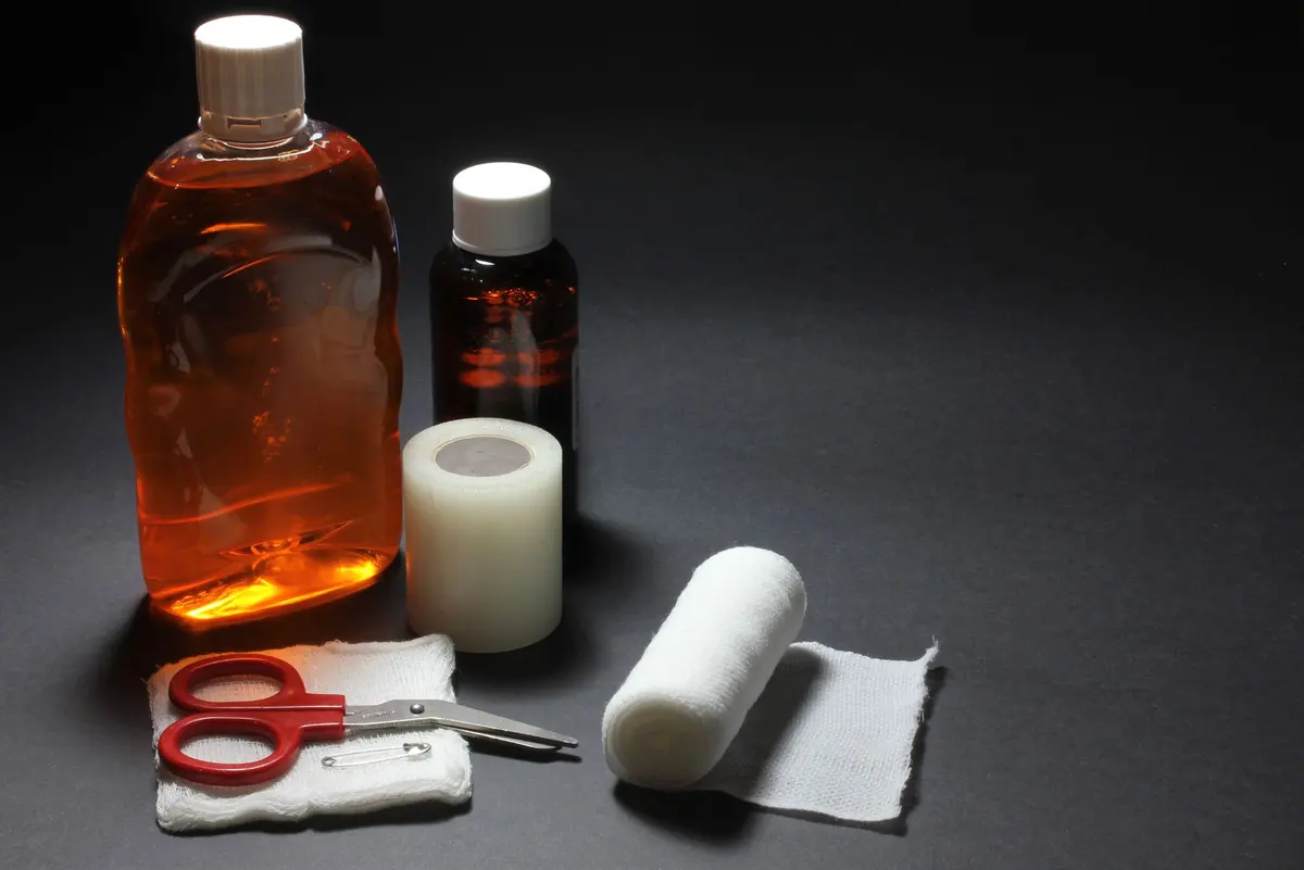 Materiale per medicazioni su un fondo scuro: un flacone di disinfettante, bende, un rotolo di cerotto e forbici