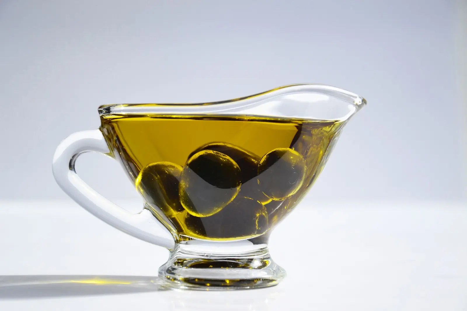 Salsiera di vetro piena d'olio con olive verdi immerse