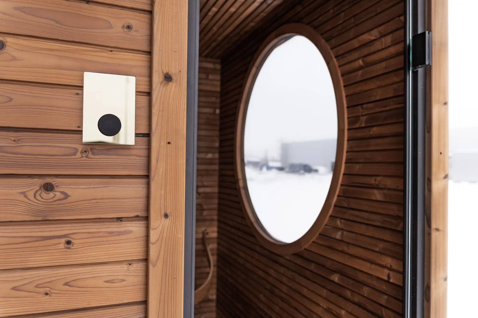 Parete di sauna in legno con un oblò che guarda la neve