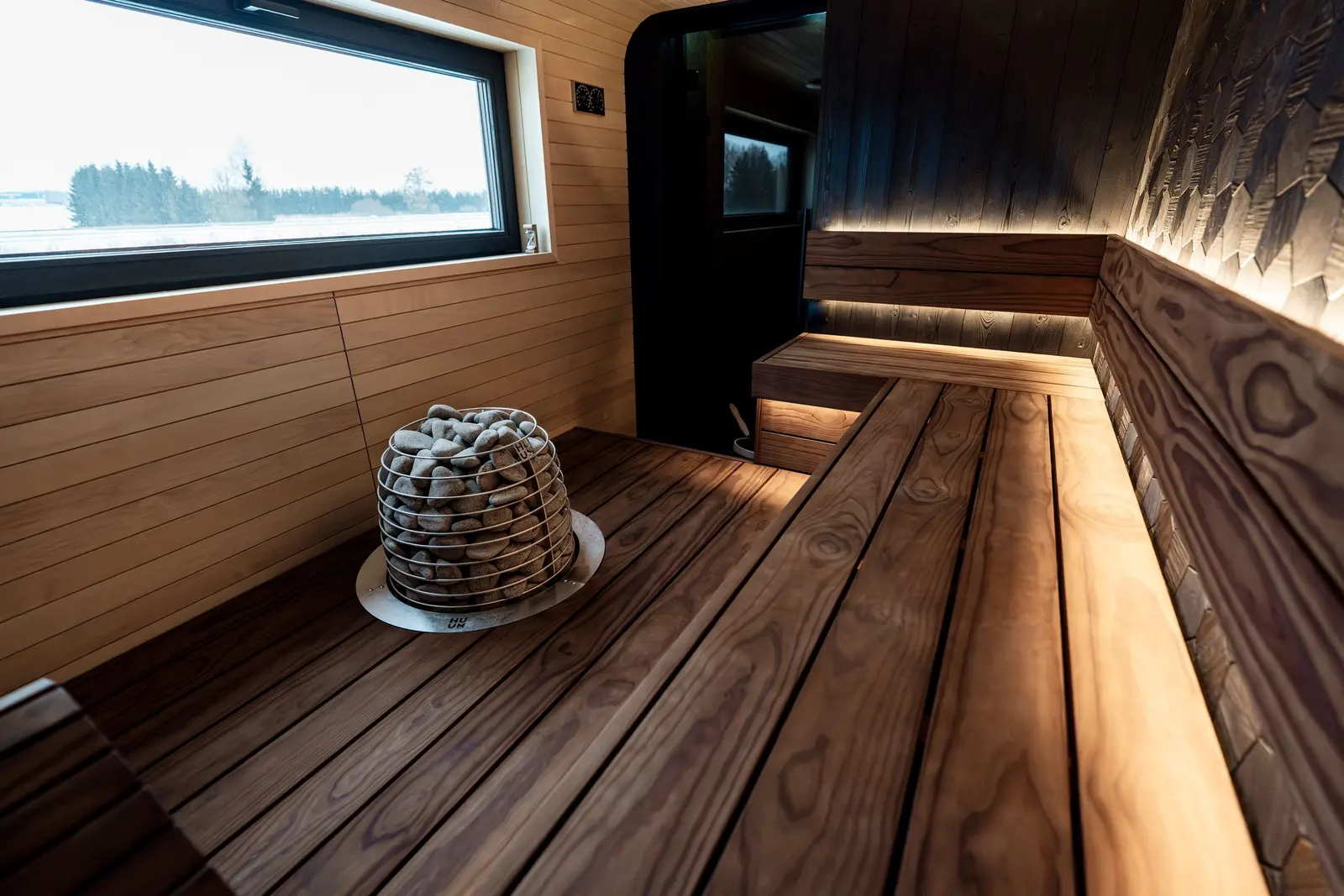 Sauna di legno con le panche e una grande vetrata sulla neve