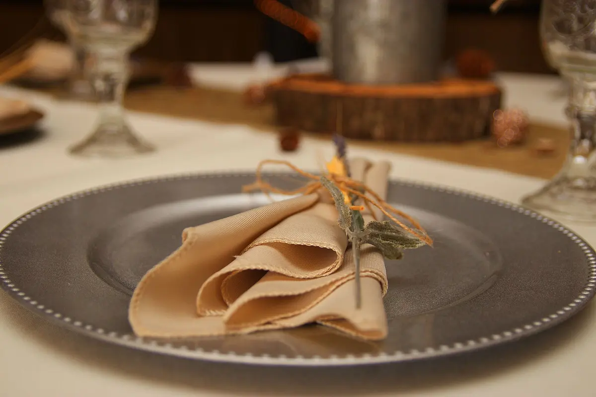 Sottopiatto argentato con il bordo di perline e un tovagliolo di lino annodato con lo spago