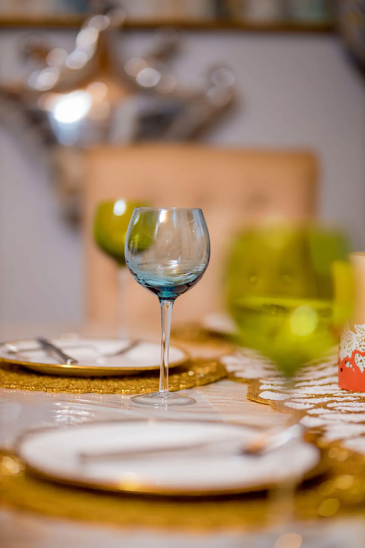 Calici colorati azzurro e verde su una tavola apparecchiata con sottopiatti dorati
