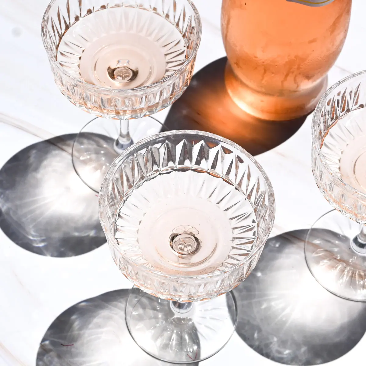 Coppe da champagne in cristallo lavorato con vino rosato, ombre nette al sole