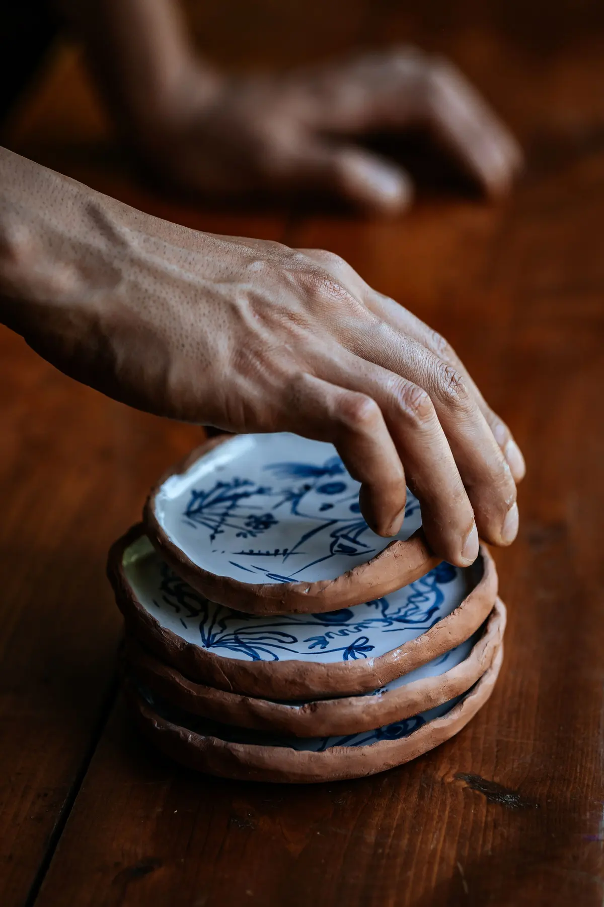 Una mano appoggia un piatto di ceramica con decori blu su una pila di piatti uguali