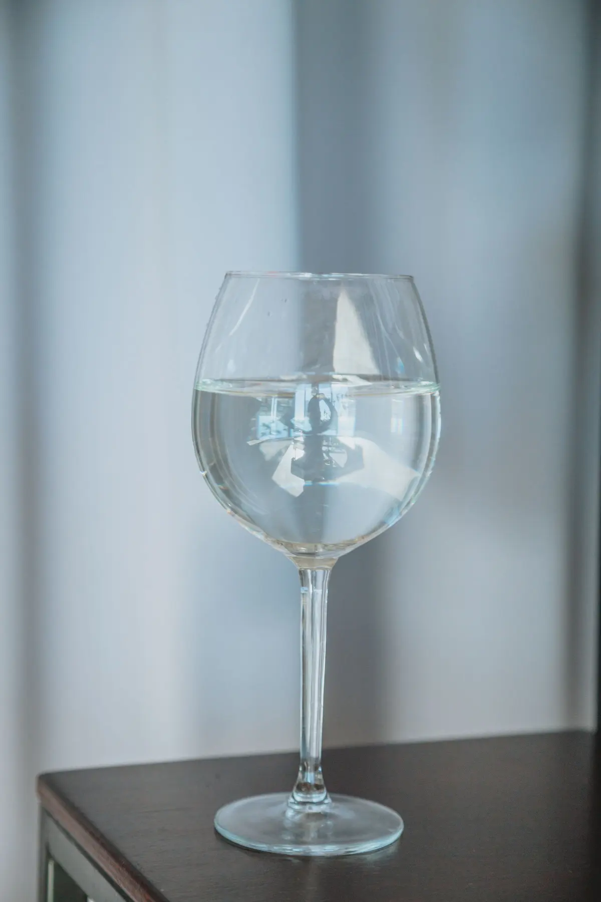 Calice liscio a stelo lungo pieno d'acqua su un mobile scuro, luce morbida