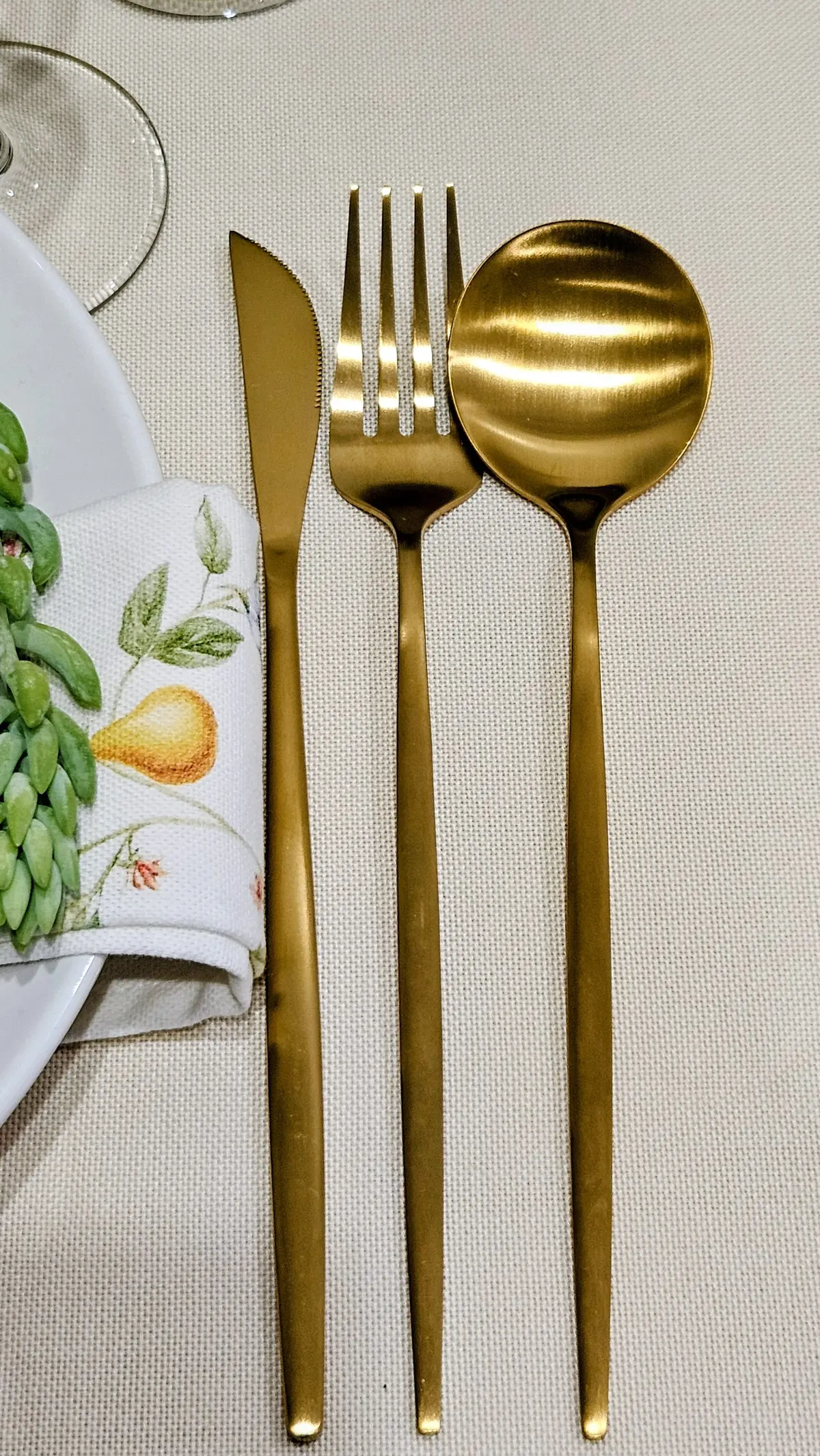 Coltello, forchetta e cucchiaio dorati opachi dal manico sottile appoggiati su una tovaglia