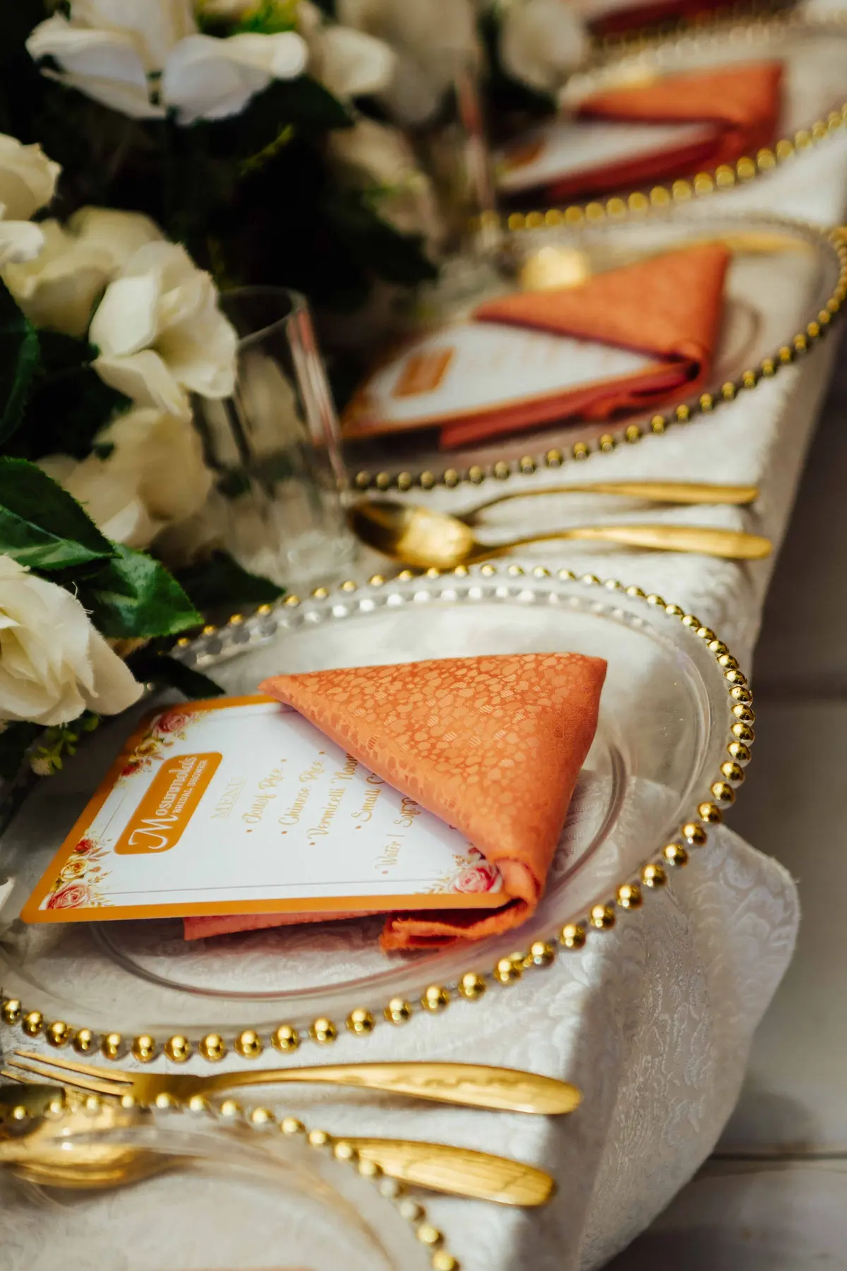 Sottopiatti dorati con il bordo di perline e tovaglioli arancio piegati sopra