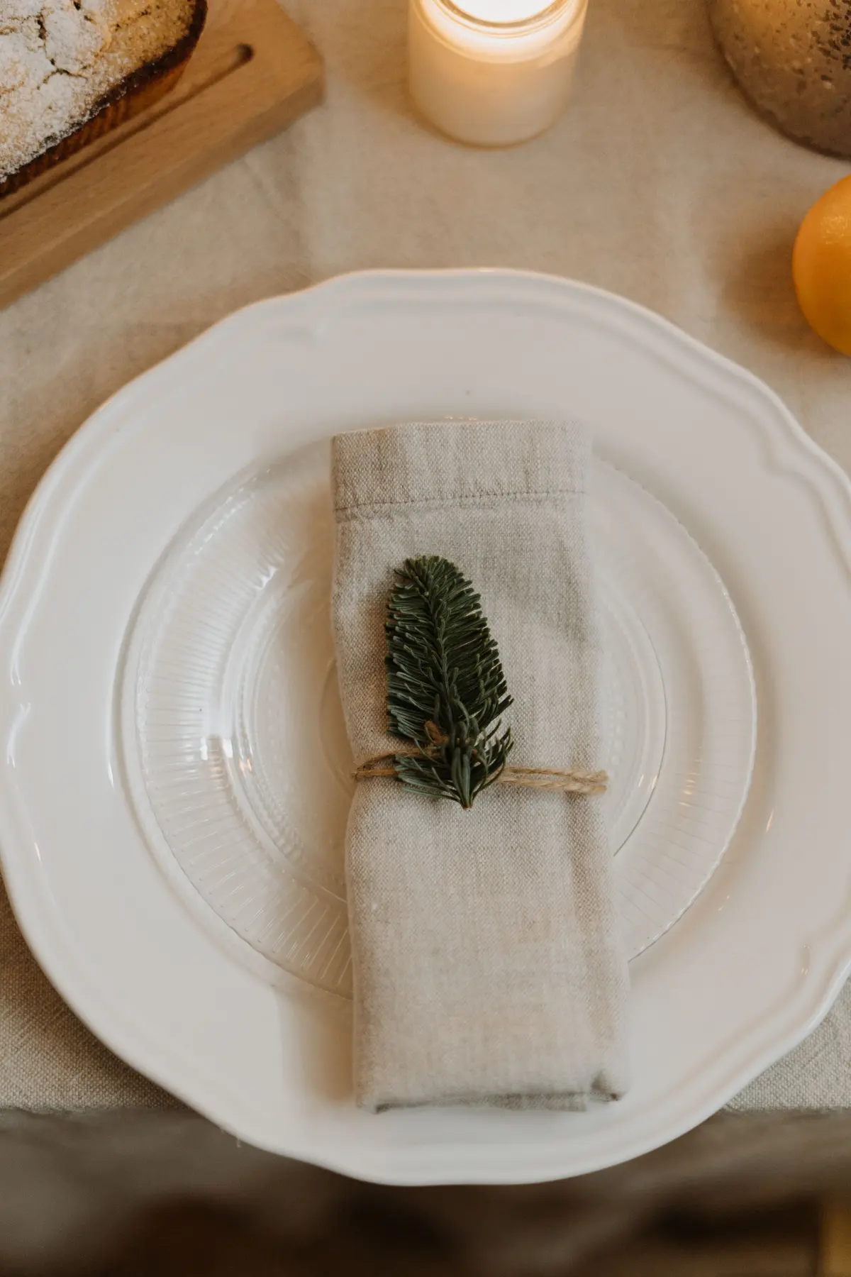 Piatto bianco con il bordo smerlato e un tovagliolo di lino legato con un rametto verde
