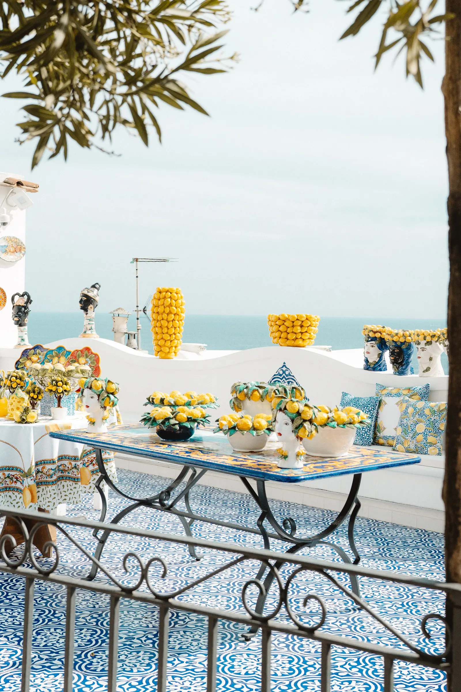Una terrazza sul mare con il pavimento di maioliche blu e un tavolo apparecchiato con limoni e ceramiche