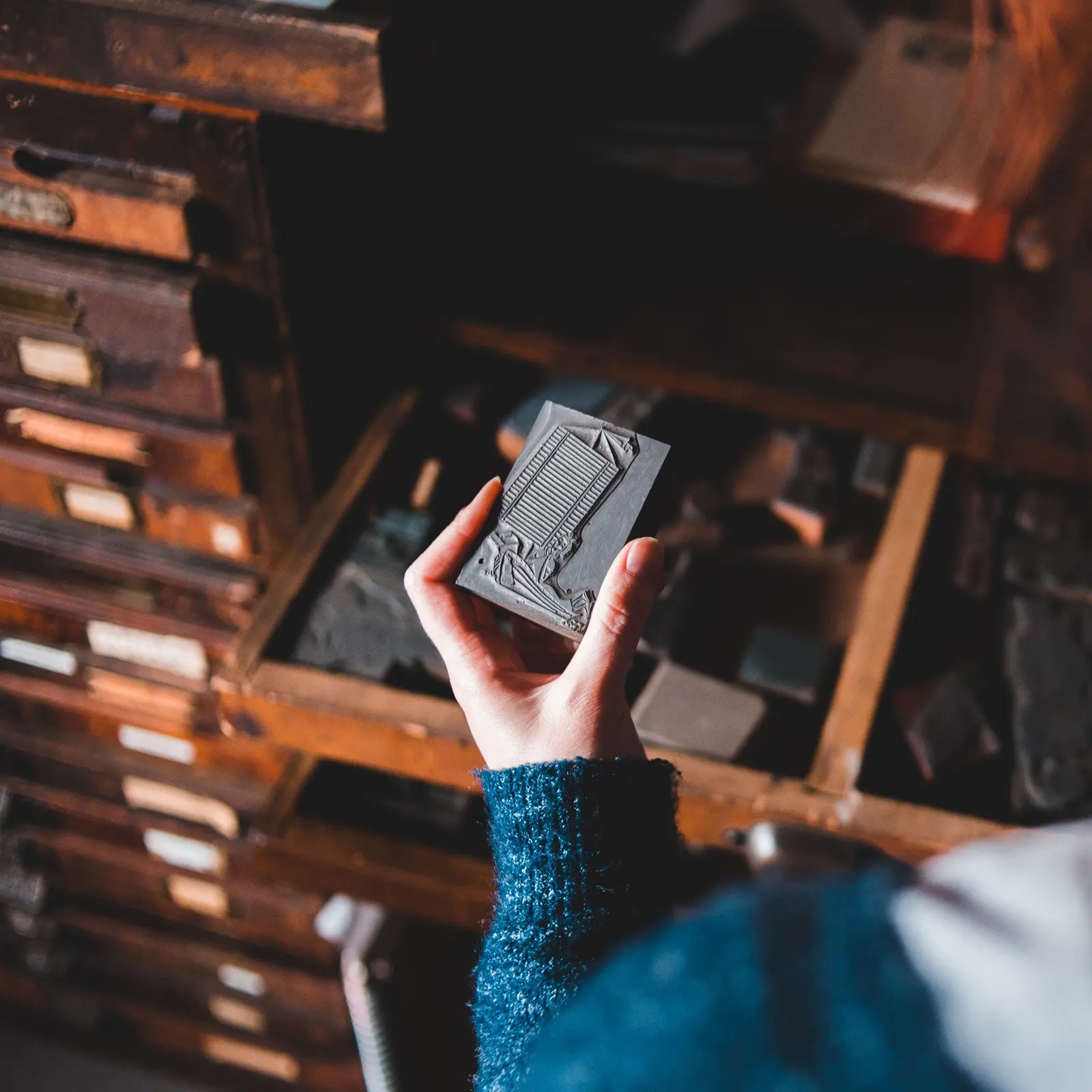 Una mano prende un cliché in metallo da un cassetto di una vecchia cassettiera tipografica in legno
