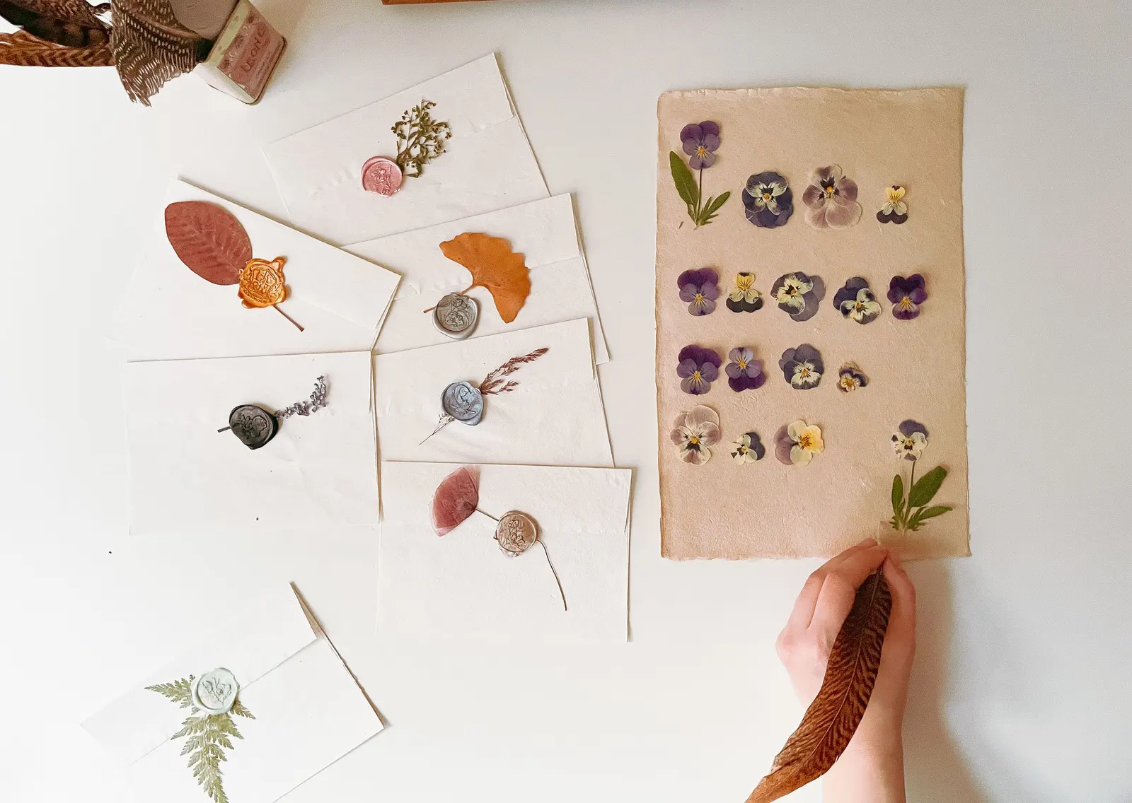 Buste fatte a mano chiuse da sigilli di ceralacca, con foglie e fiori pressati, e una mano che tiene una piuma