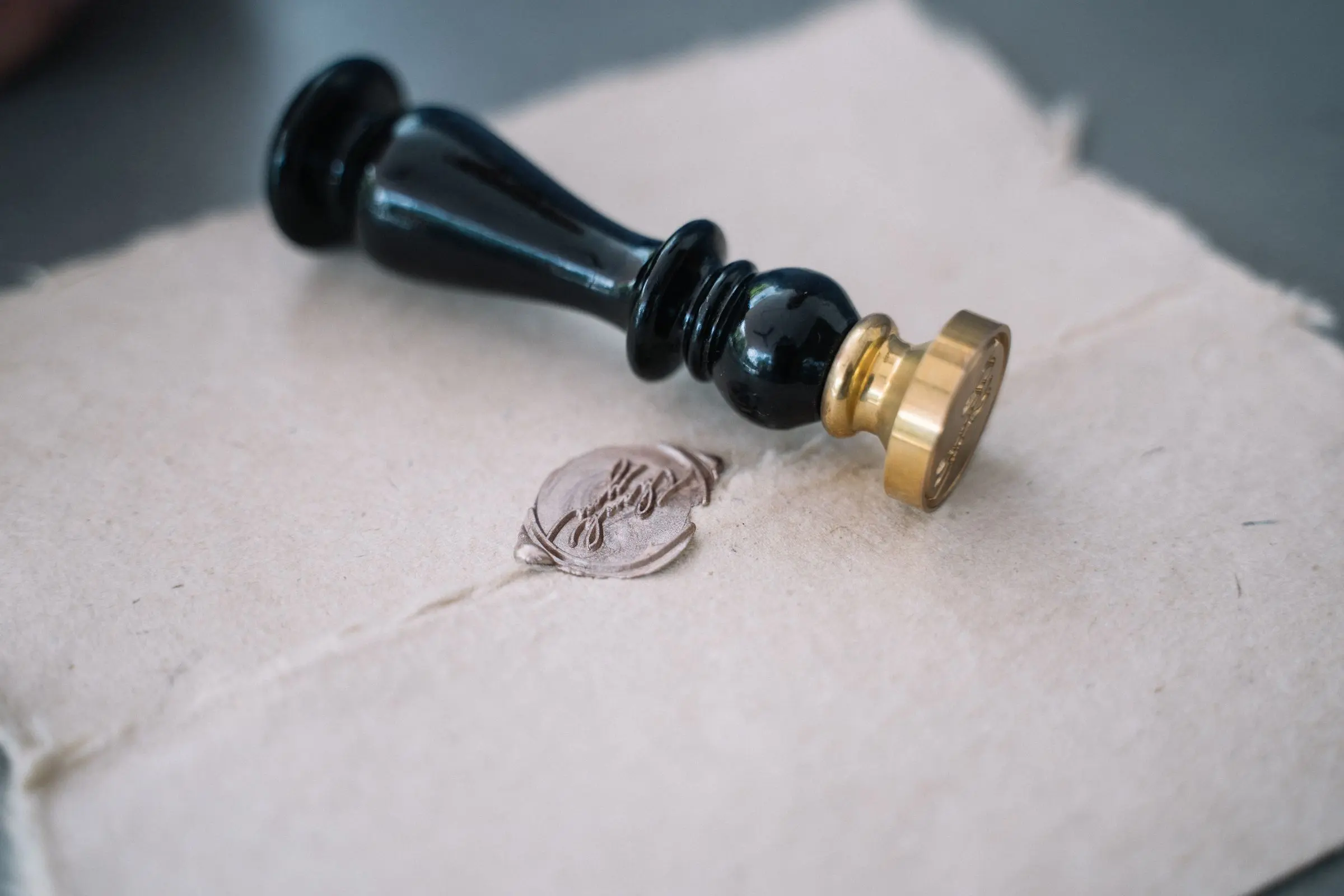 Un timbro da ceralacca nero con la testa d'ottone appoggiato su un foglio di carta di cotone fatta a mano, accanto al sigillo appena impresso