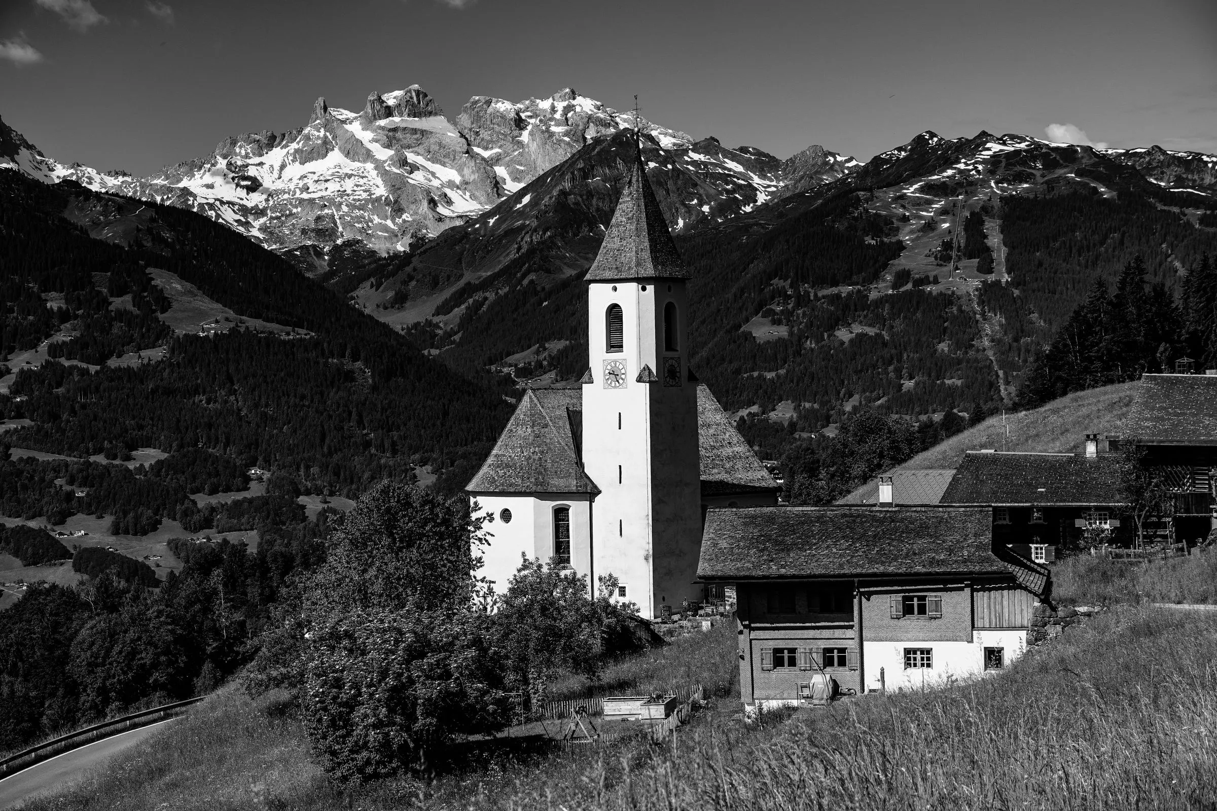 Chiesa con il campanile bianco in un paese alpino, montagne innevate dietro, in bianco e nero