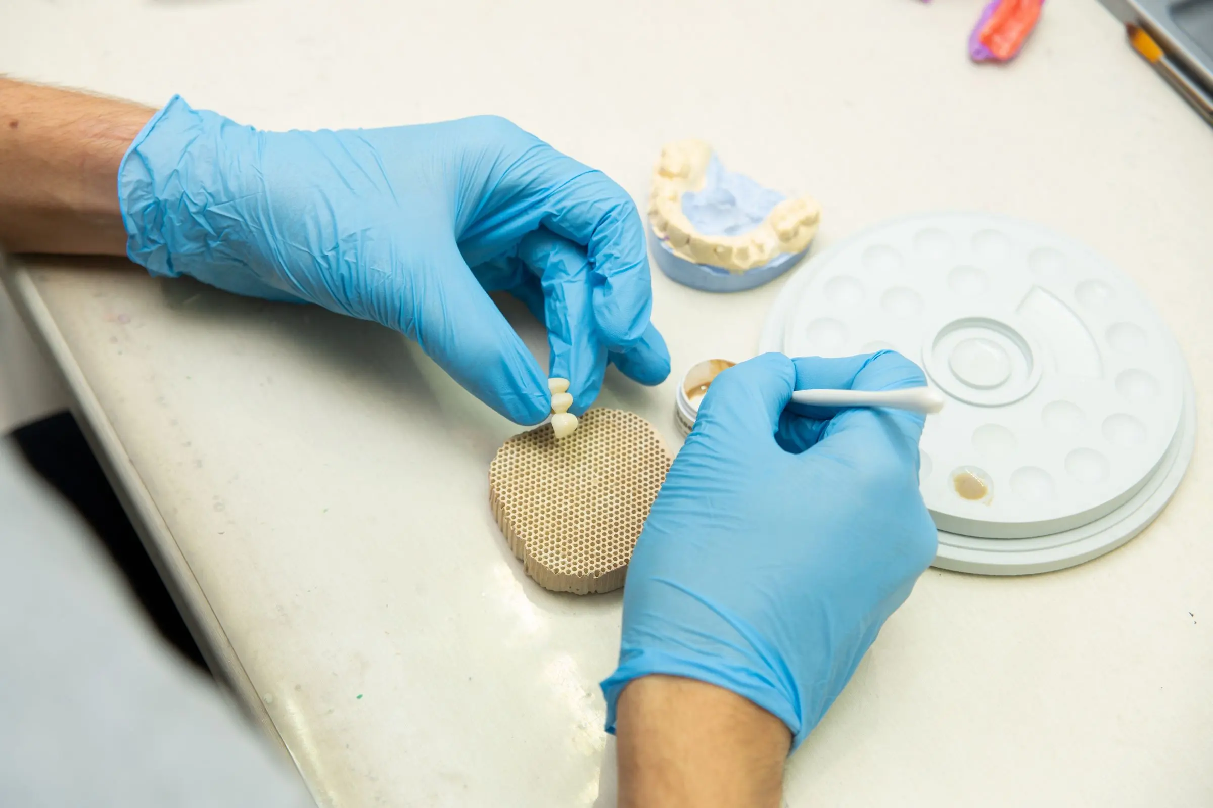 Un odontotecnico stratifica la ceramica con il pennello su un elemento, al banco