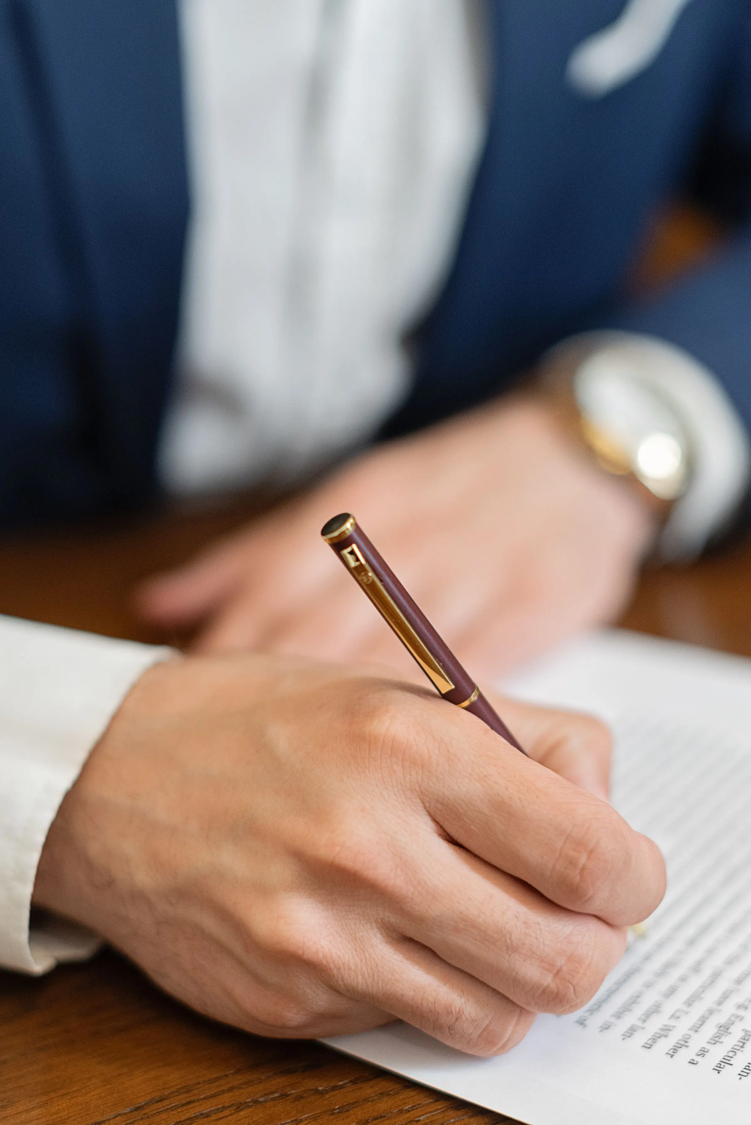 Una mano firma un contratto con la stilografica su un tavolo di legno