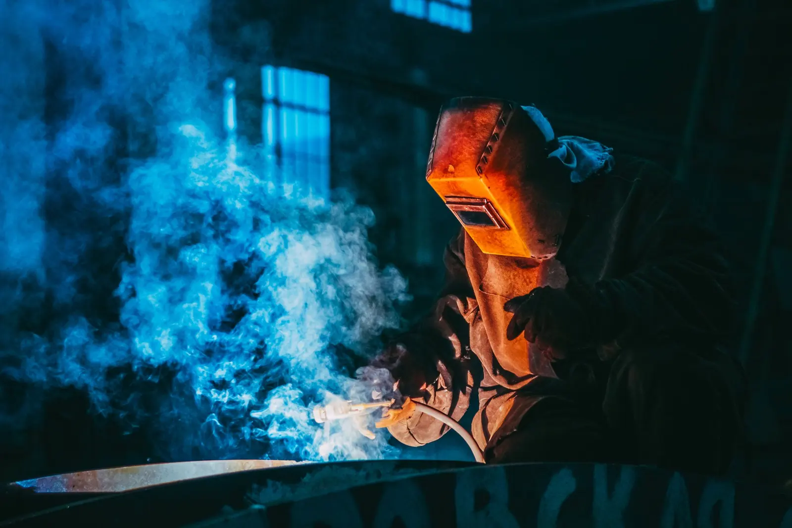 Un saldatore con la maschera al lavoro, nel fumo azzurro della saldatura