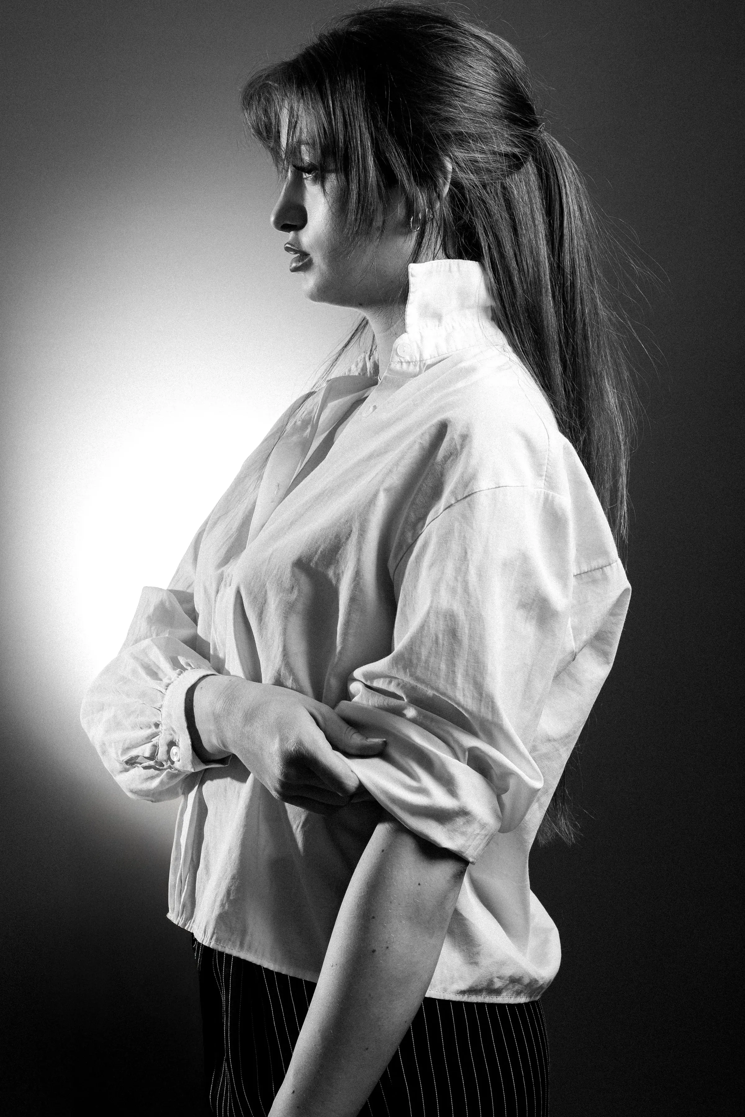 Ritratto di profilo in bianco e nero: capelli raccolti in una coda bassa, camicia bianca, luce di studio