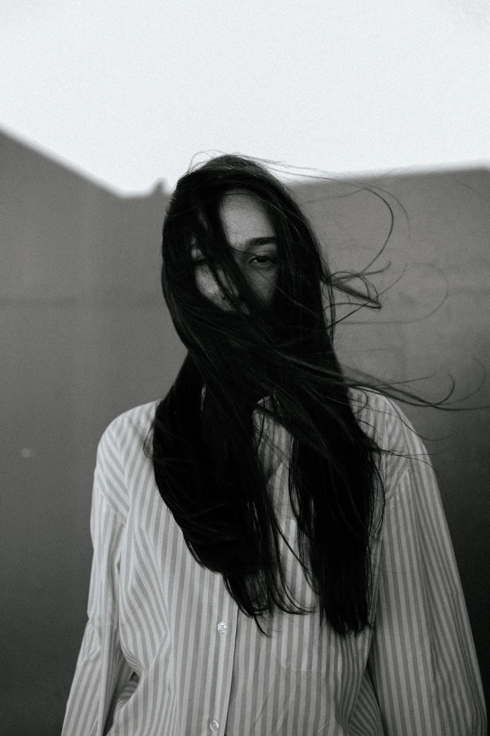 Capelli neri lunghi spinti dal vento davanti al volto, camicia a righe