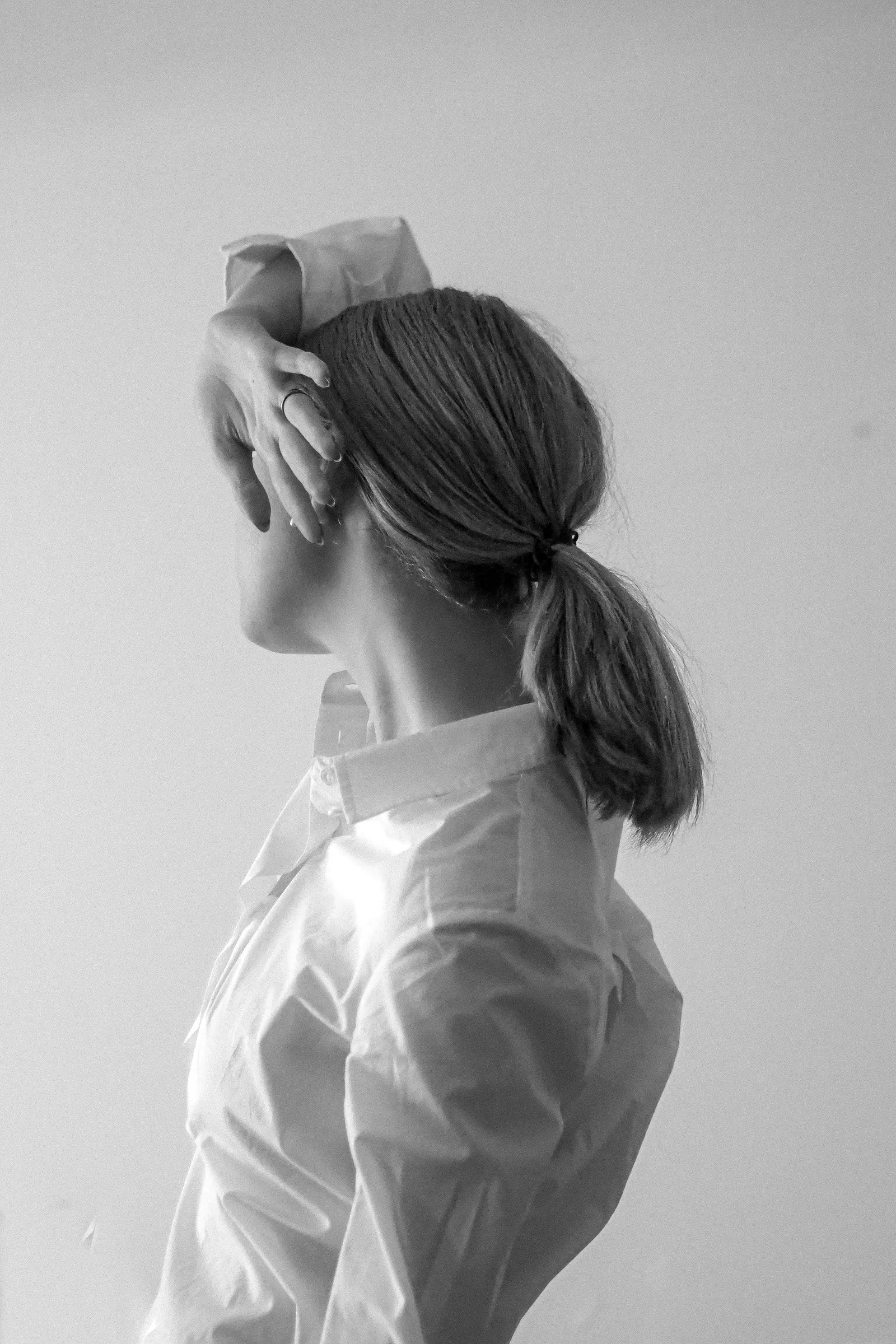 Donna di spalle con coda bassa, una mano tra i capelli, toni chiari