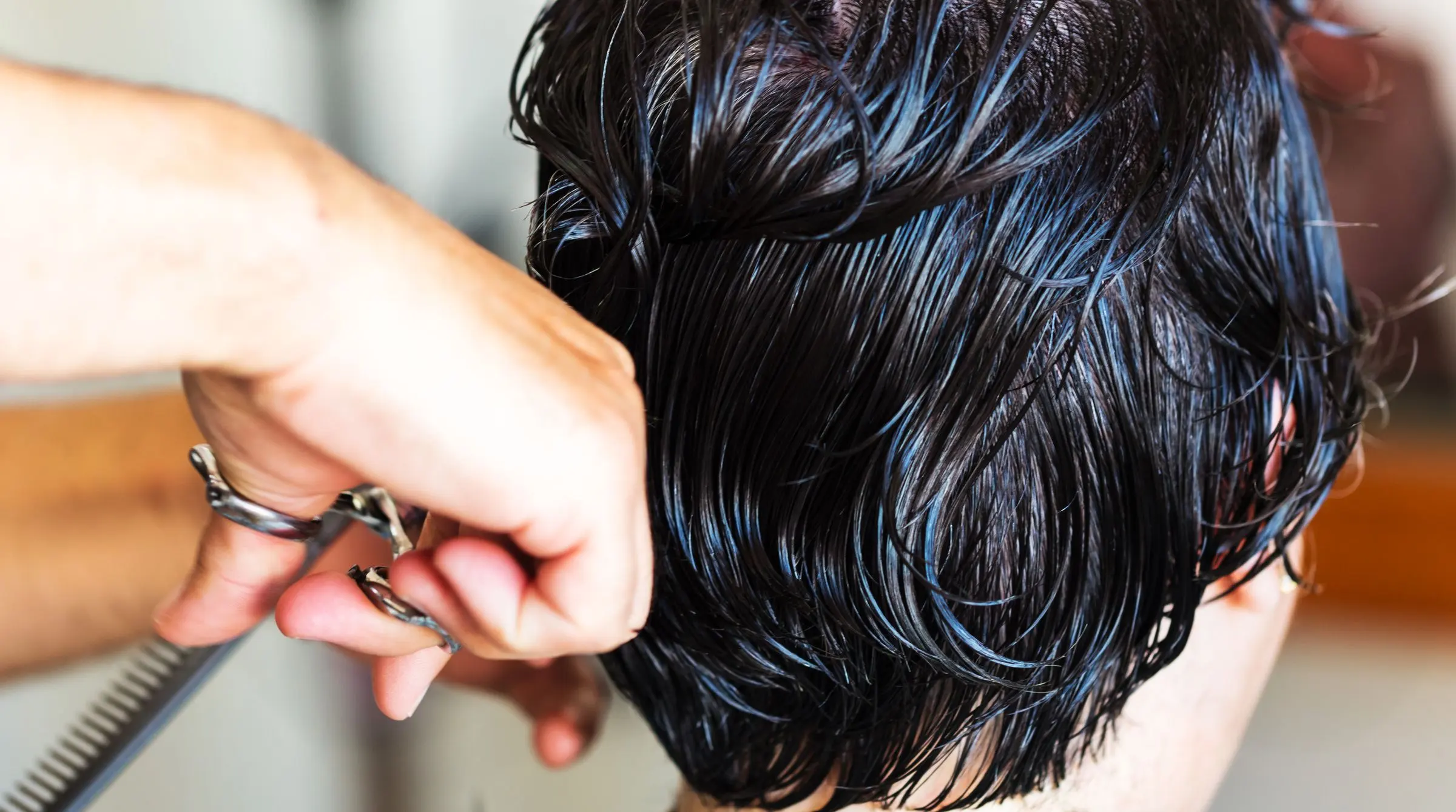 Forbici che rifiniscono un taglio corto su capelli scuri bagnati, in primo piano